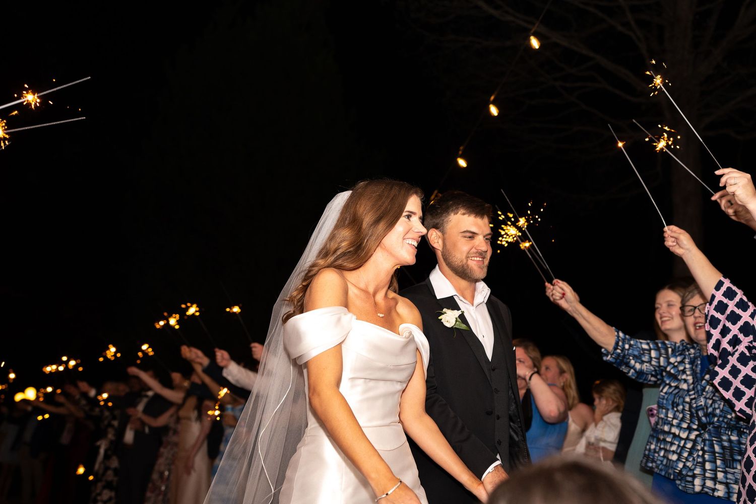 Wedding guests wave sparklers during a nighttime celebration.
