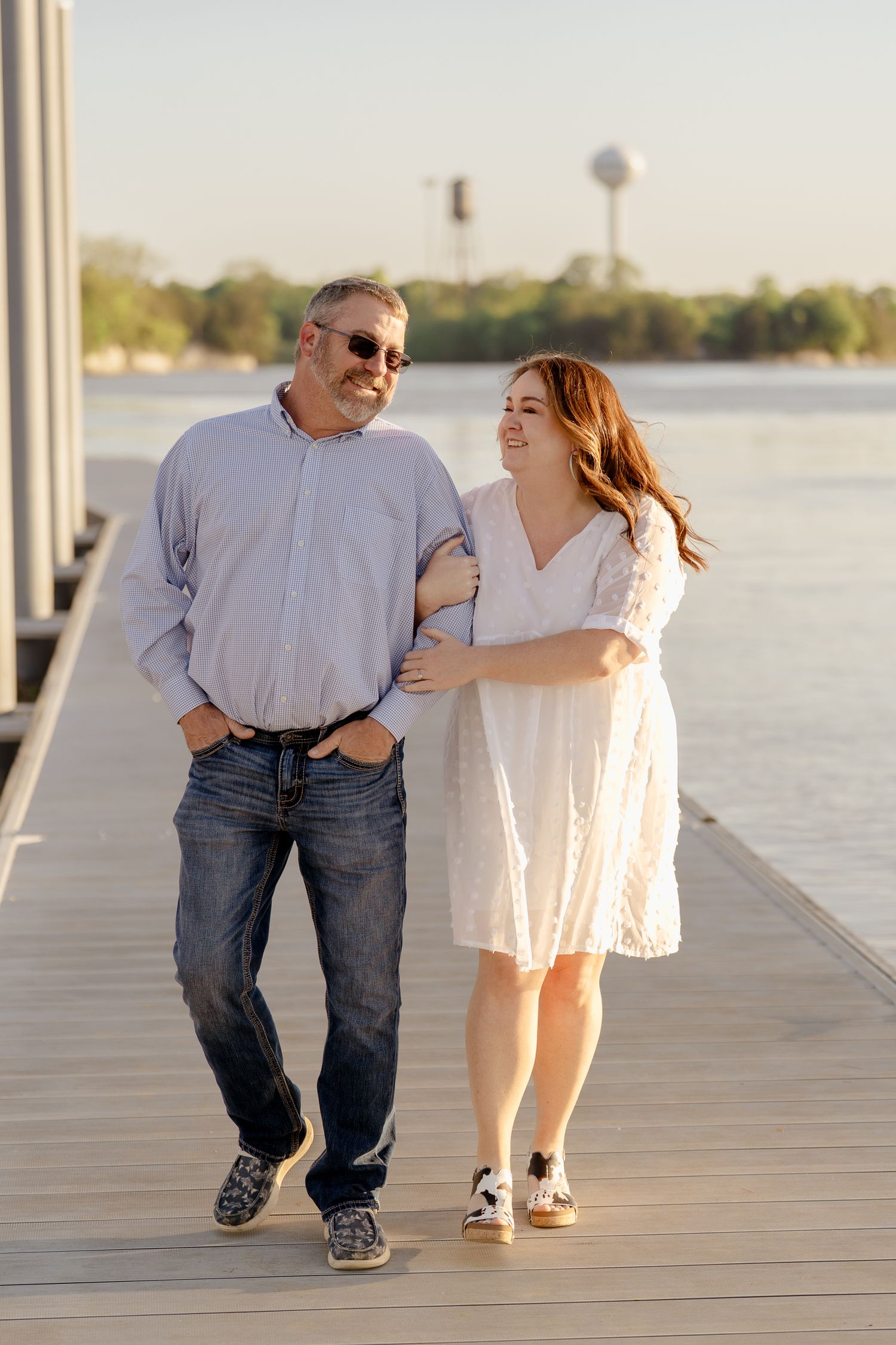Two people share a joyful moment walking together on a waterfront boardwalk at sunset.