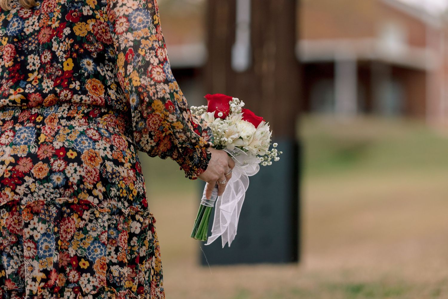 Bride in colorful floral dress holding a bridal bouquet of red roses and white flowers with ribbon.