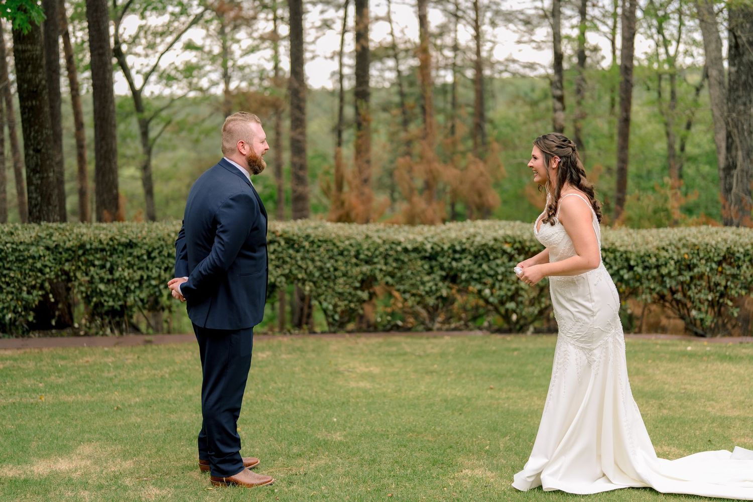 Bride and groom share an emotional first look moment on a green lawn surrounded by trees.