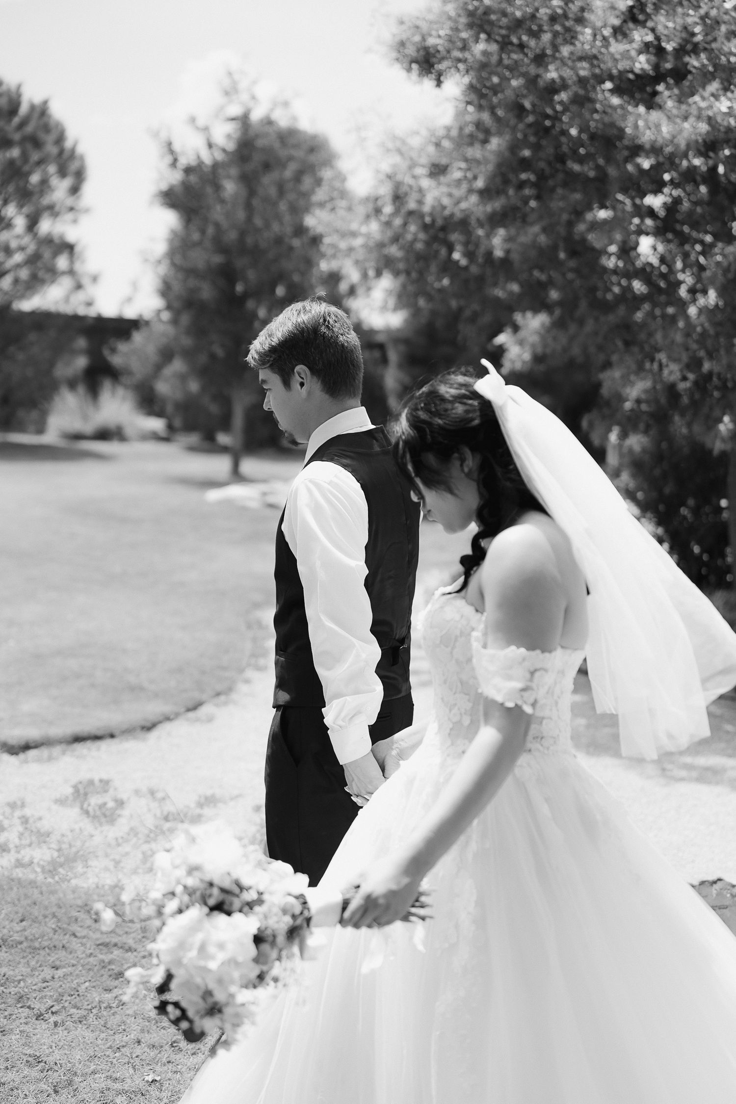Black and white photo of bride and groom holding hands outdoors on their wedding day.