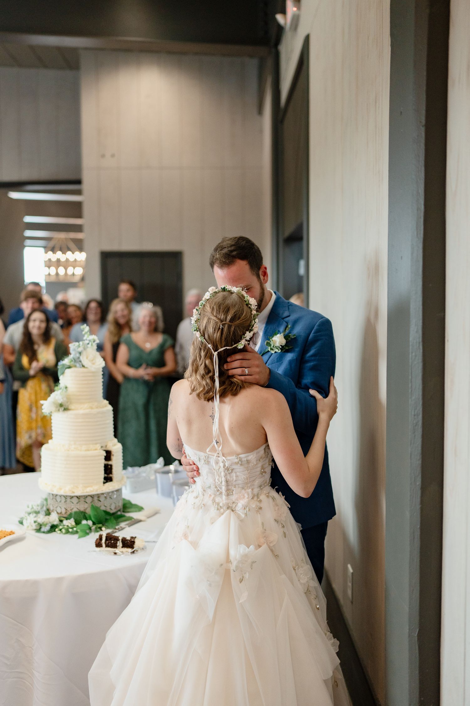 A couple shares their first dance at a wedding reception while guests watch near elegant white tiered cakes.