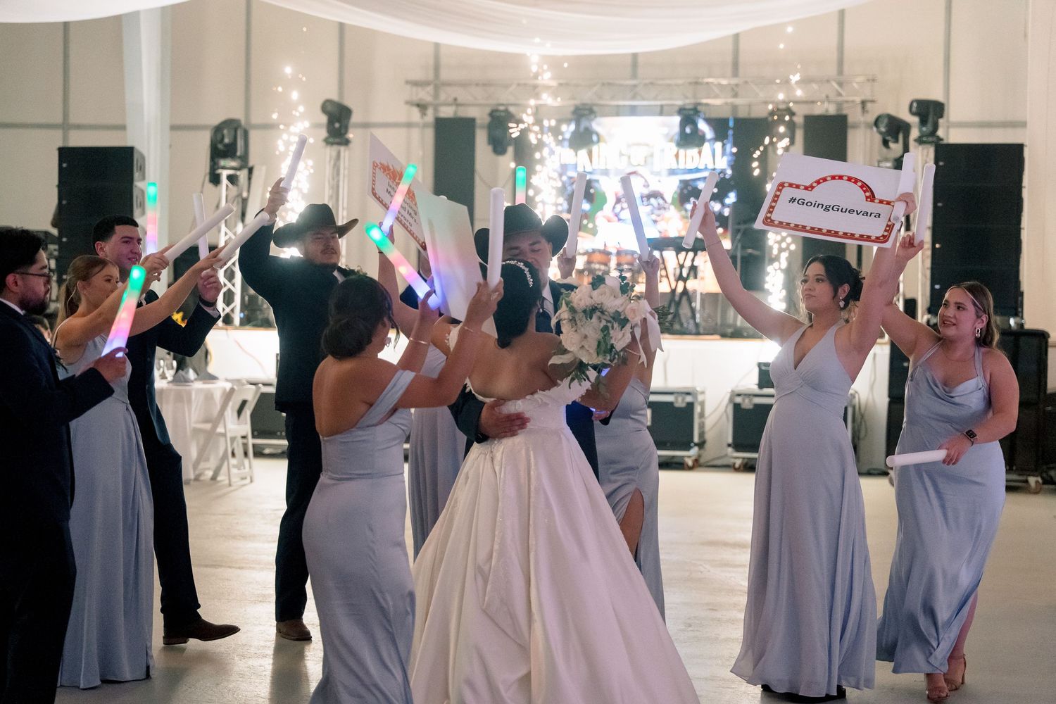 Wedding party dancing in a ballroom with bridesmaids in gray dresses and a bride in a white gown.