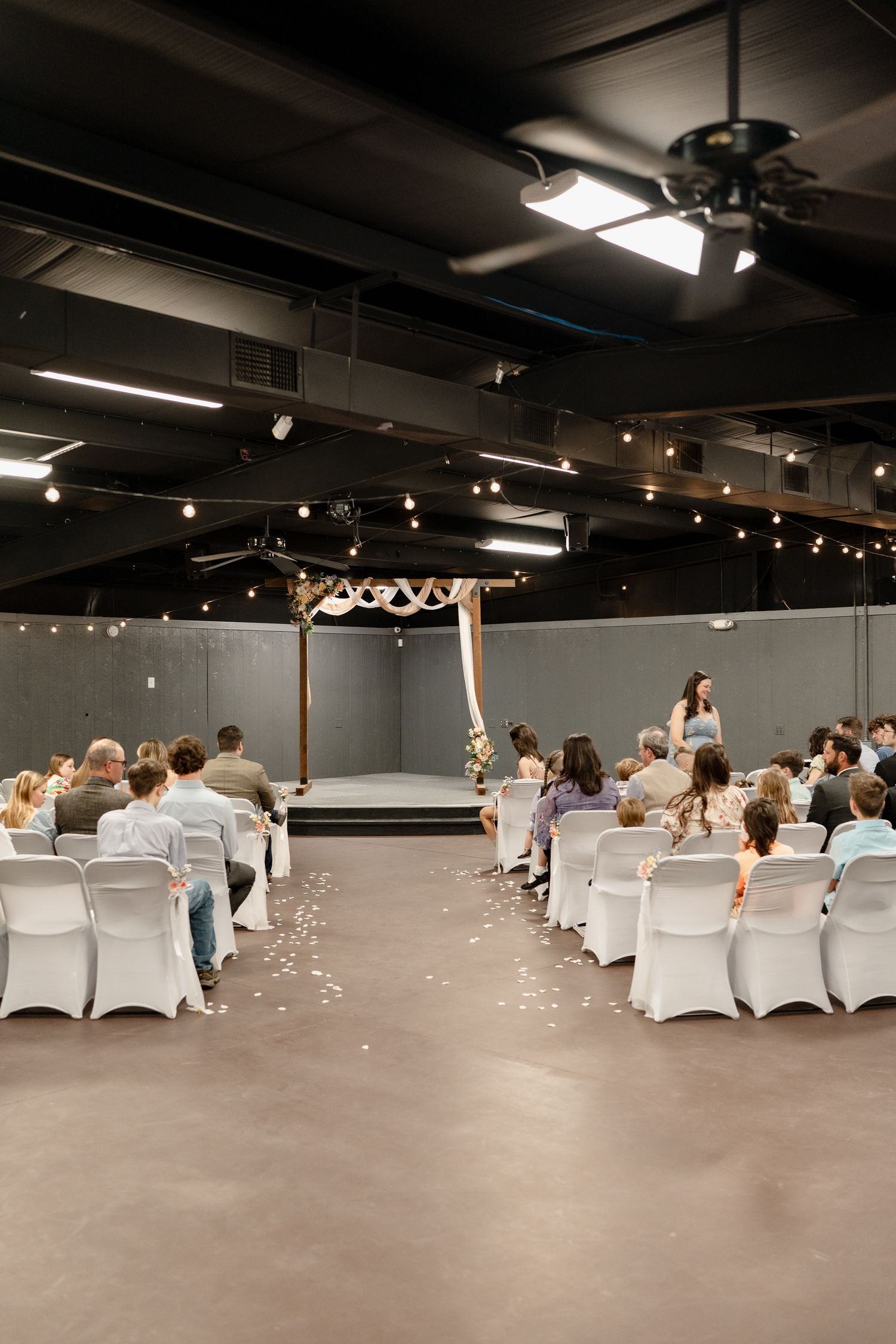 Wide panoramic view of a modern event space with white chair covers and track lighting on dark ceiling.
