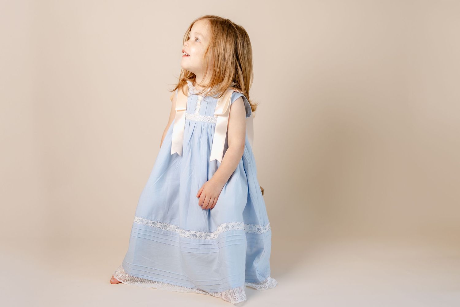Child in pale blue vintage dress posing against neutral backdrop during photo shoot.