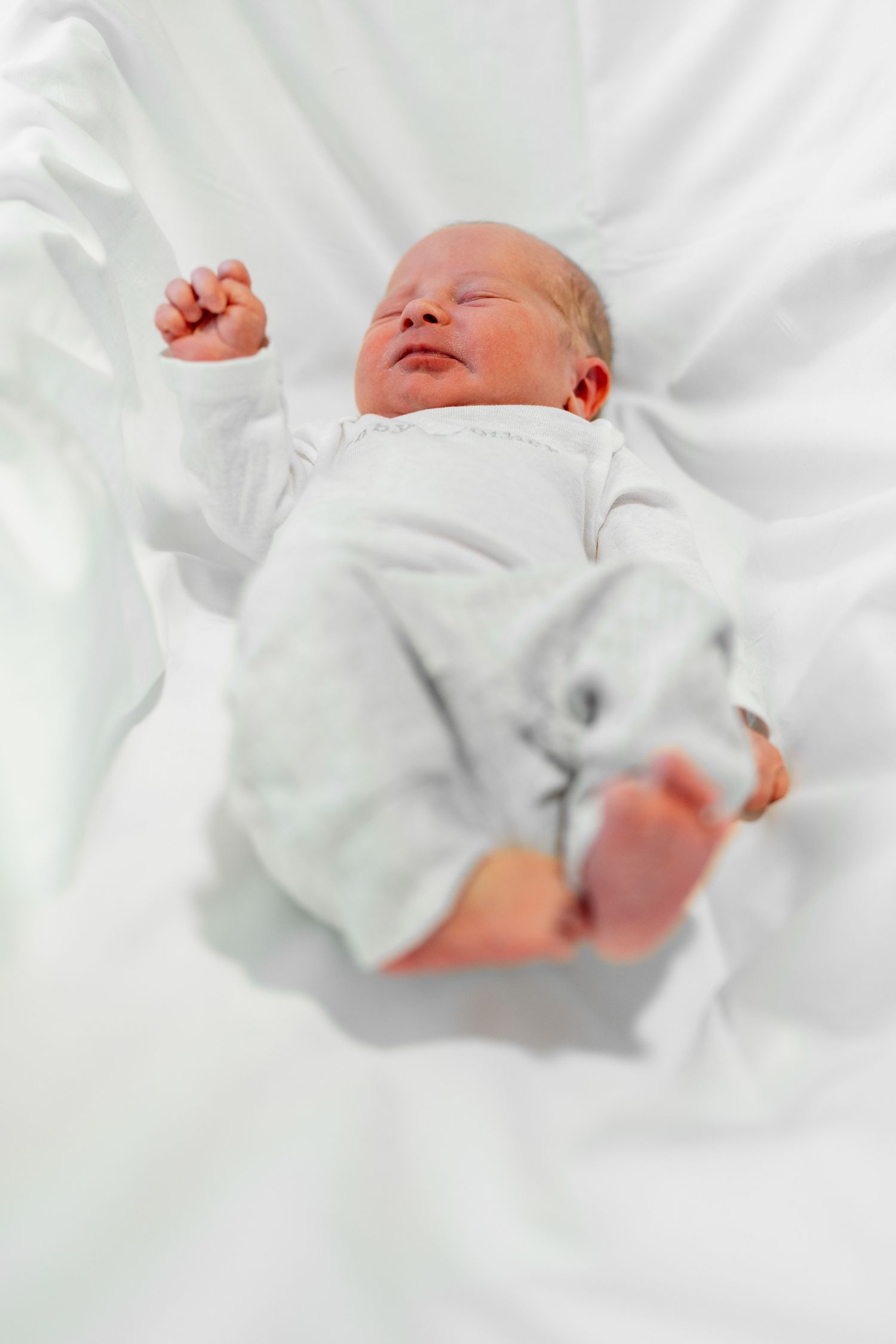 Baby dressed in white clothing resting peacefully on soft white linens.