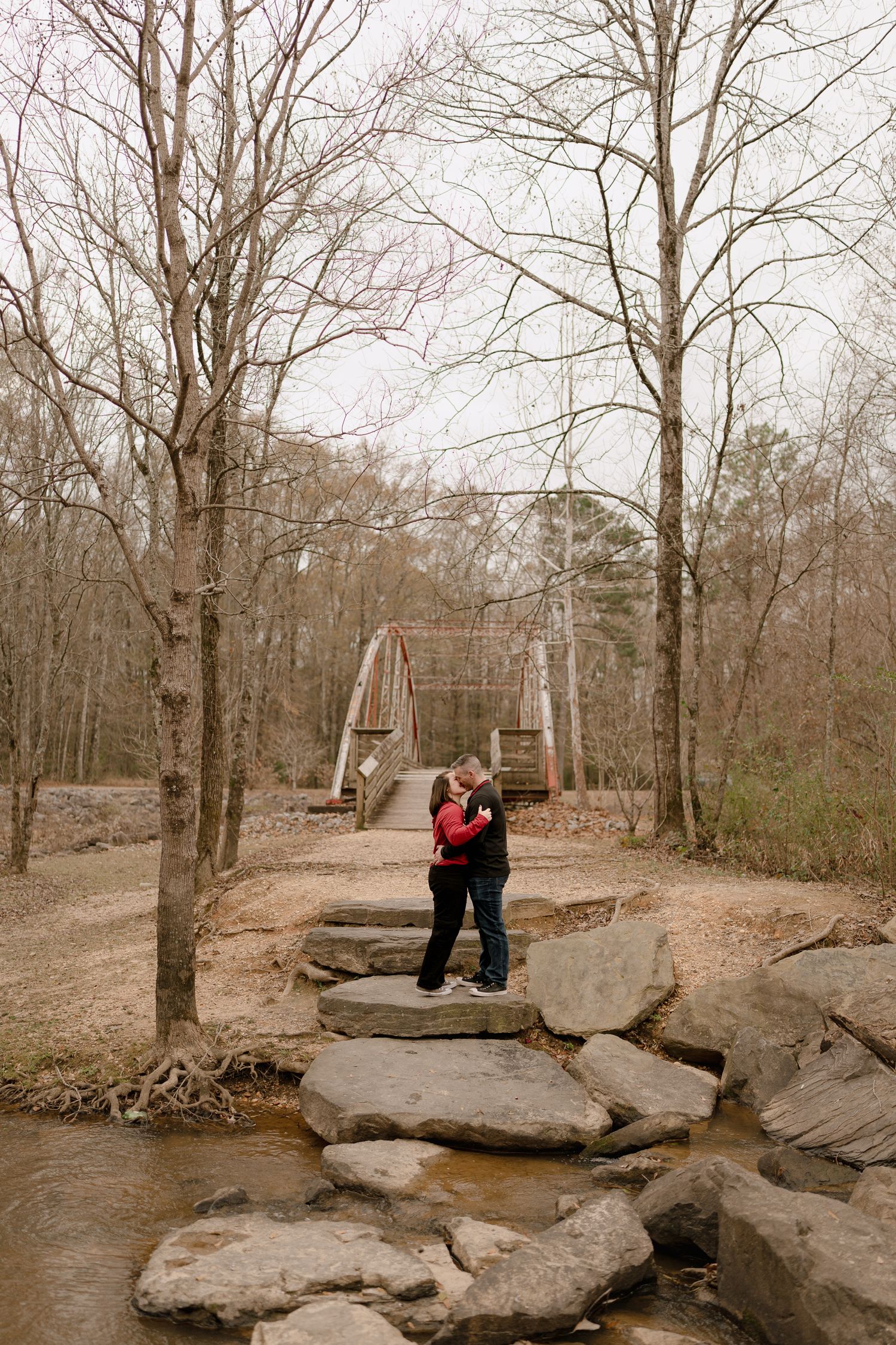 A couple poses together on large rocks in a winter forest setting.