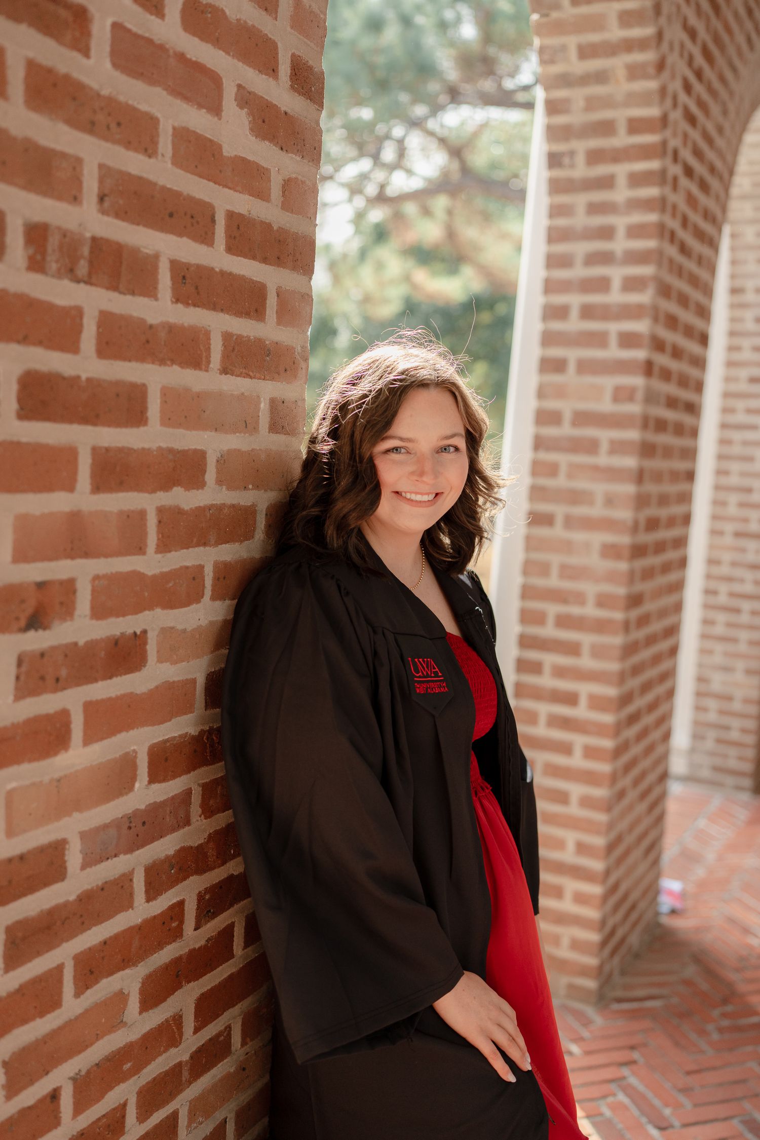 Professional graduation portrait session featuring a graduate in black cap and gown with red accents on a brick walkway.
