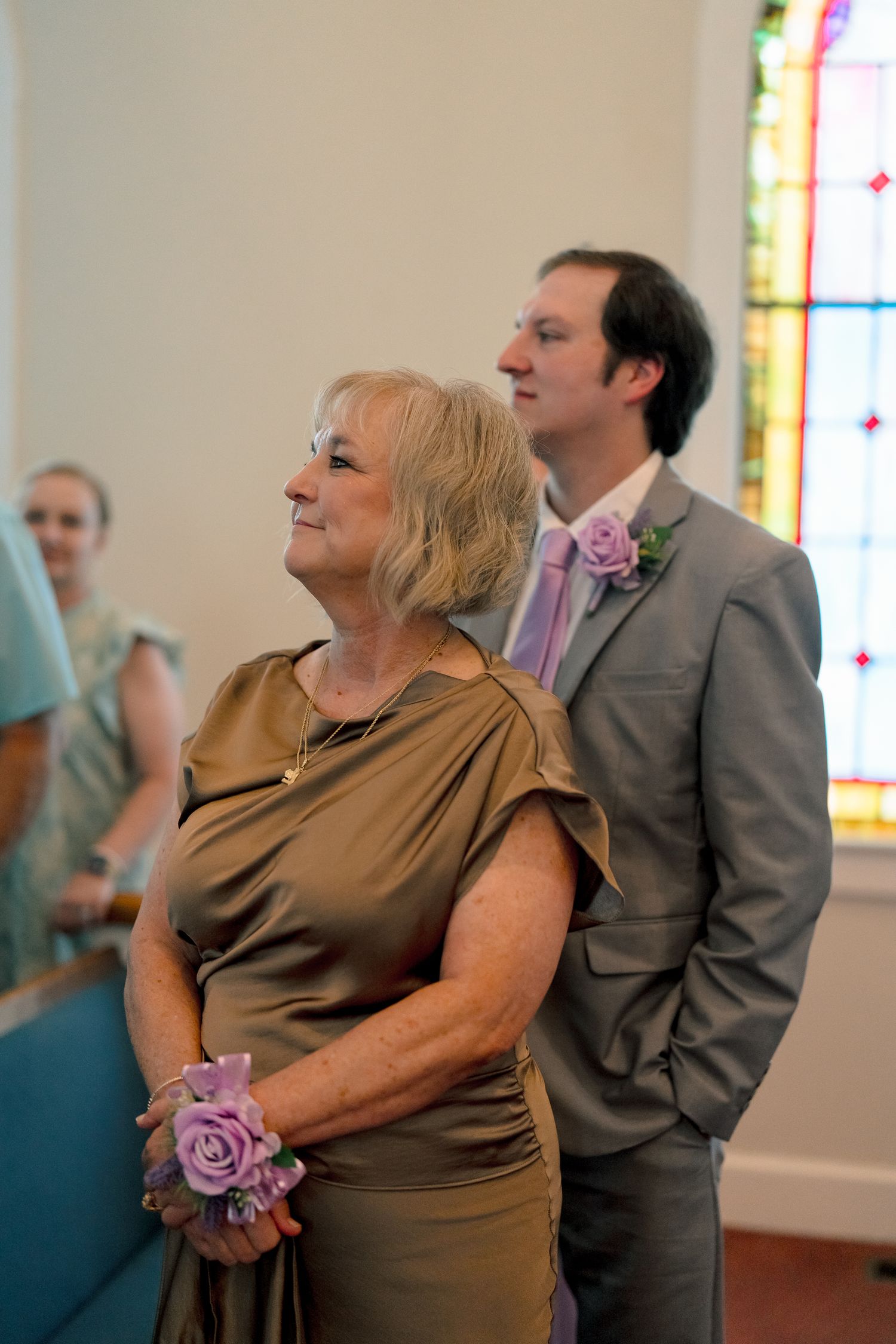 Elegant older woman with corsage and young groomsman standing in a church before wedding ceremony.