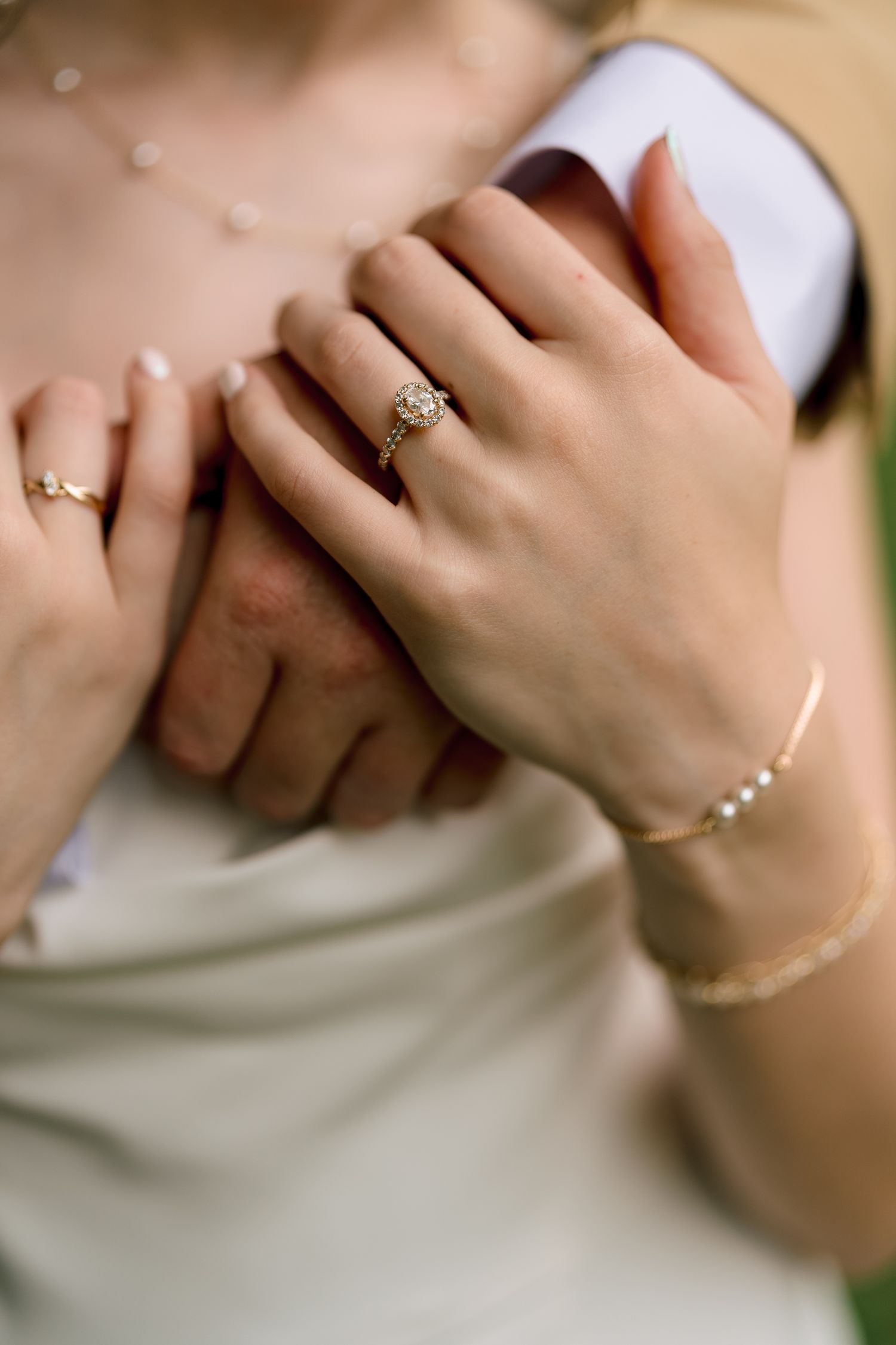 Bride wearing diamond engagement ring and pearl bracelet holding groom's hand on wedding day.