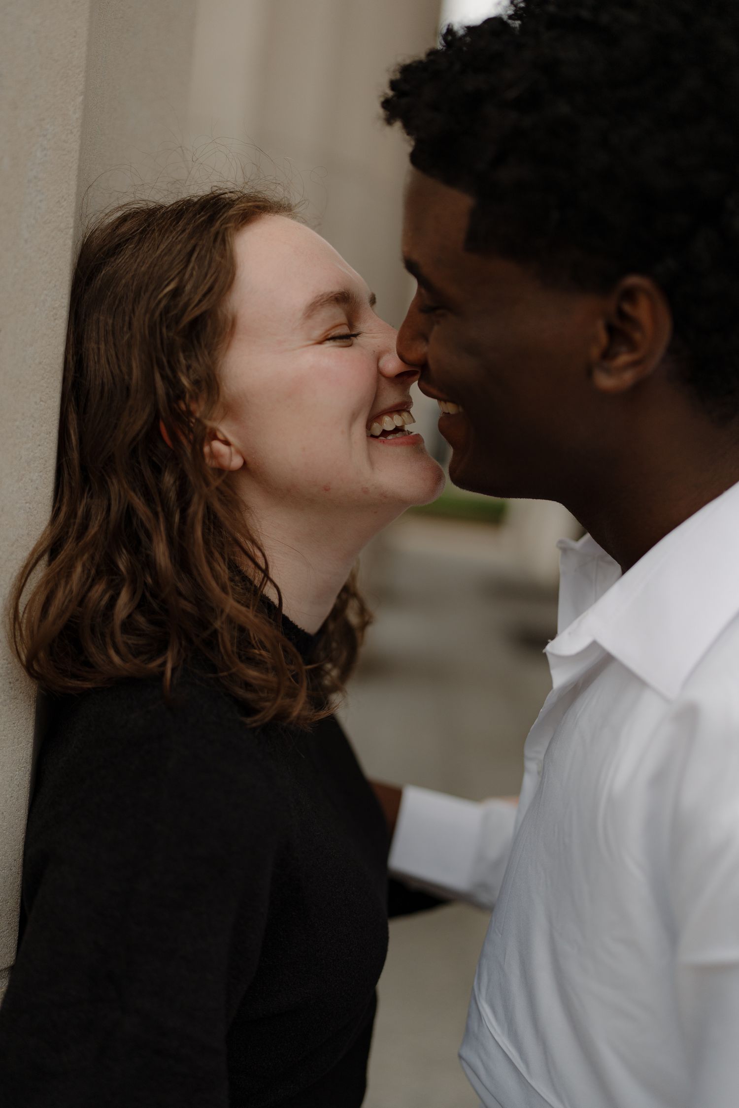 Close-up of happy interracial couple sharing a tender moment, nearly kissing against a stone column backdrop.