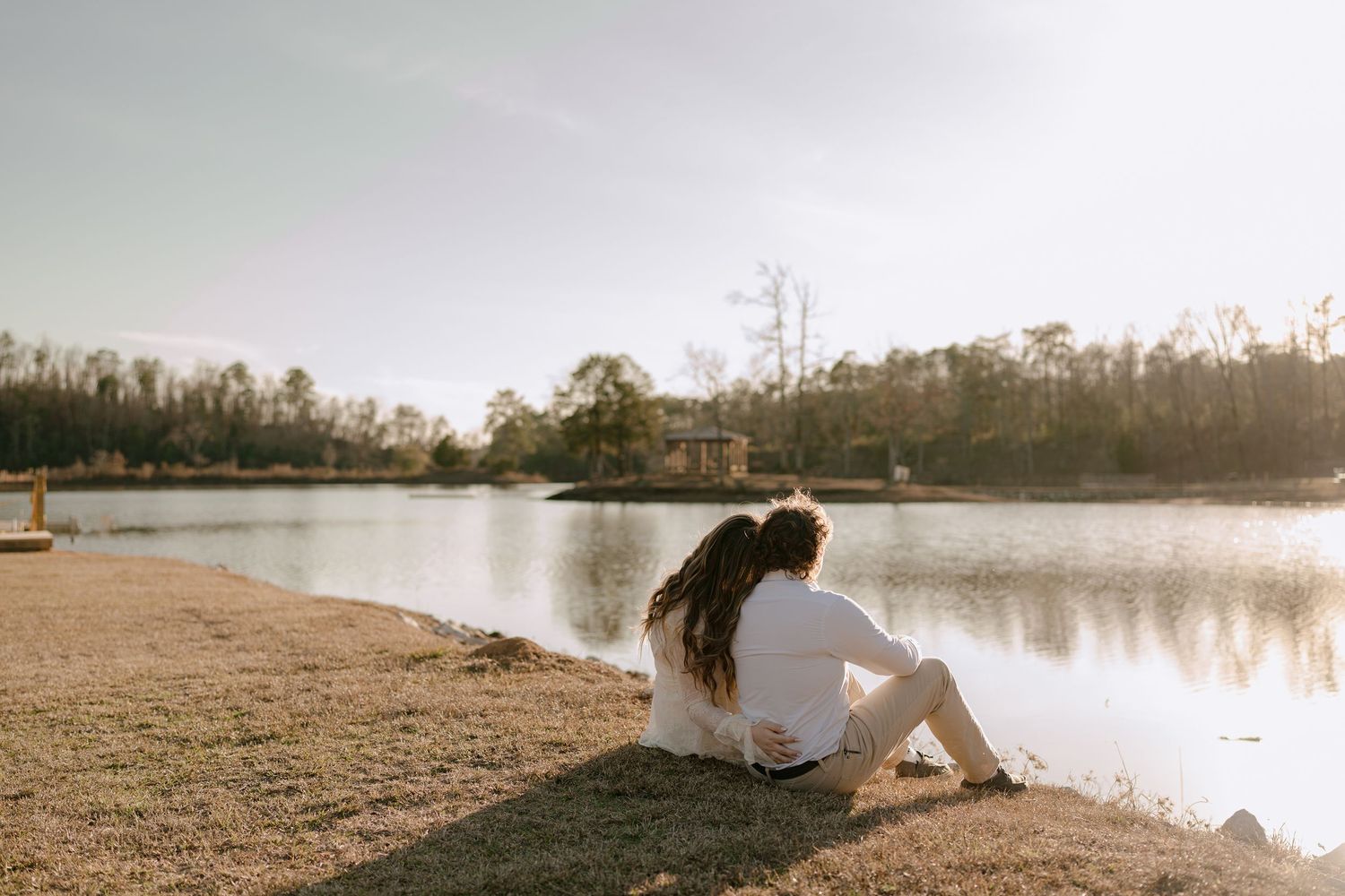 Couple sitting together by a calm lake shore, enjoying a peaceful golden hour moment outdoors.