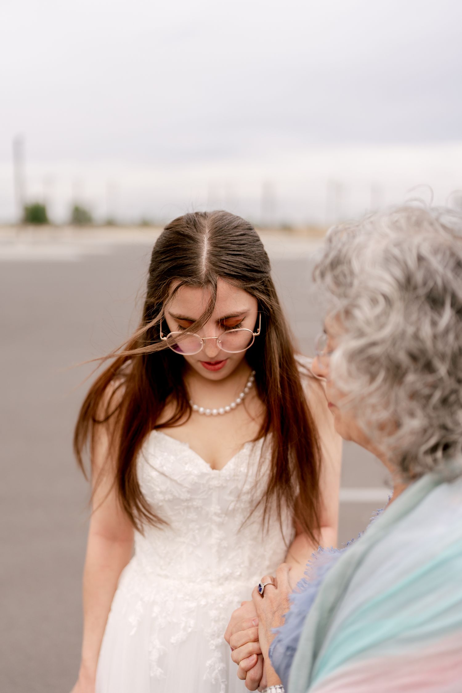 A person in a white lace wedding dress shares a tender moment with someone wearing light blue outdoors.
