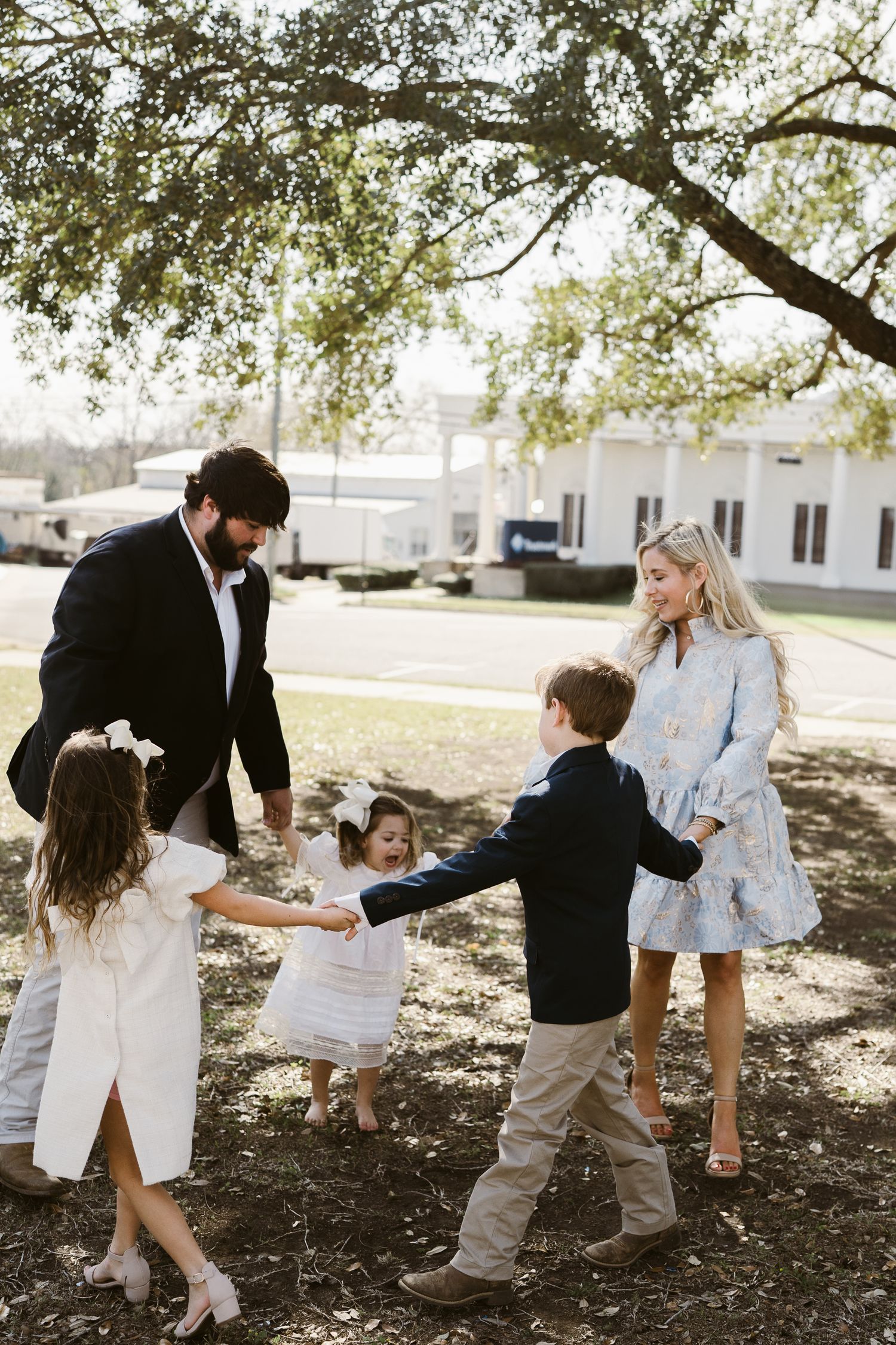 Candid family moments under a large tree with children playing and adults in casual formalwear.