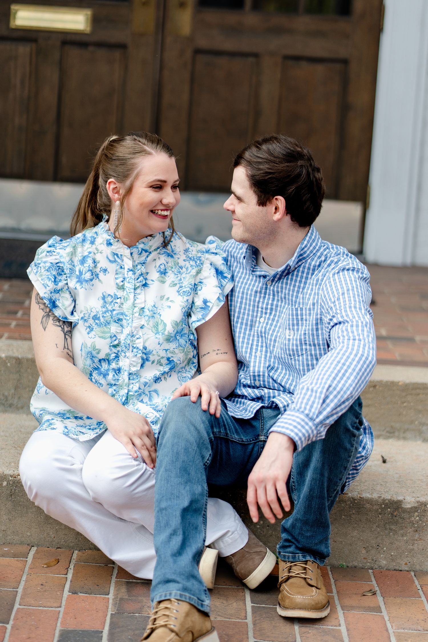 Couple in coordinating blue and white outfits share candid moments while sitting on brick steps.