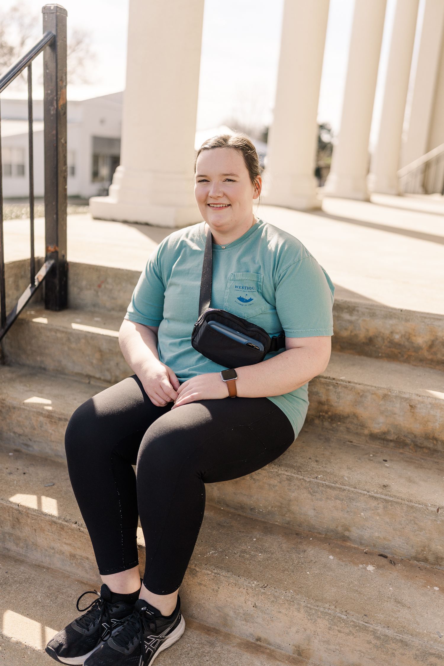 Person sitting on stone steps wearing teal shirt and black pants with a fanny pack.
