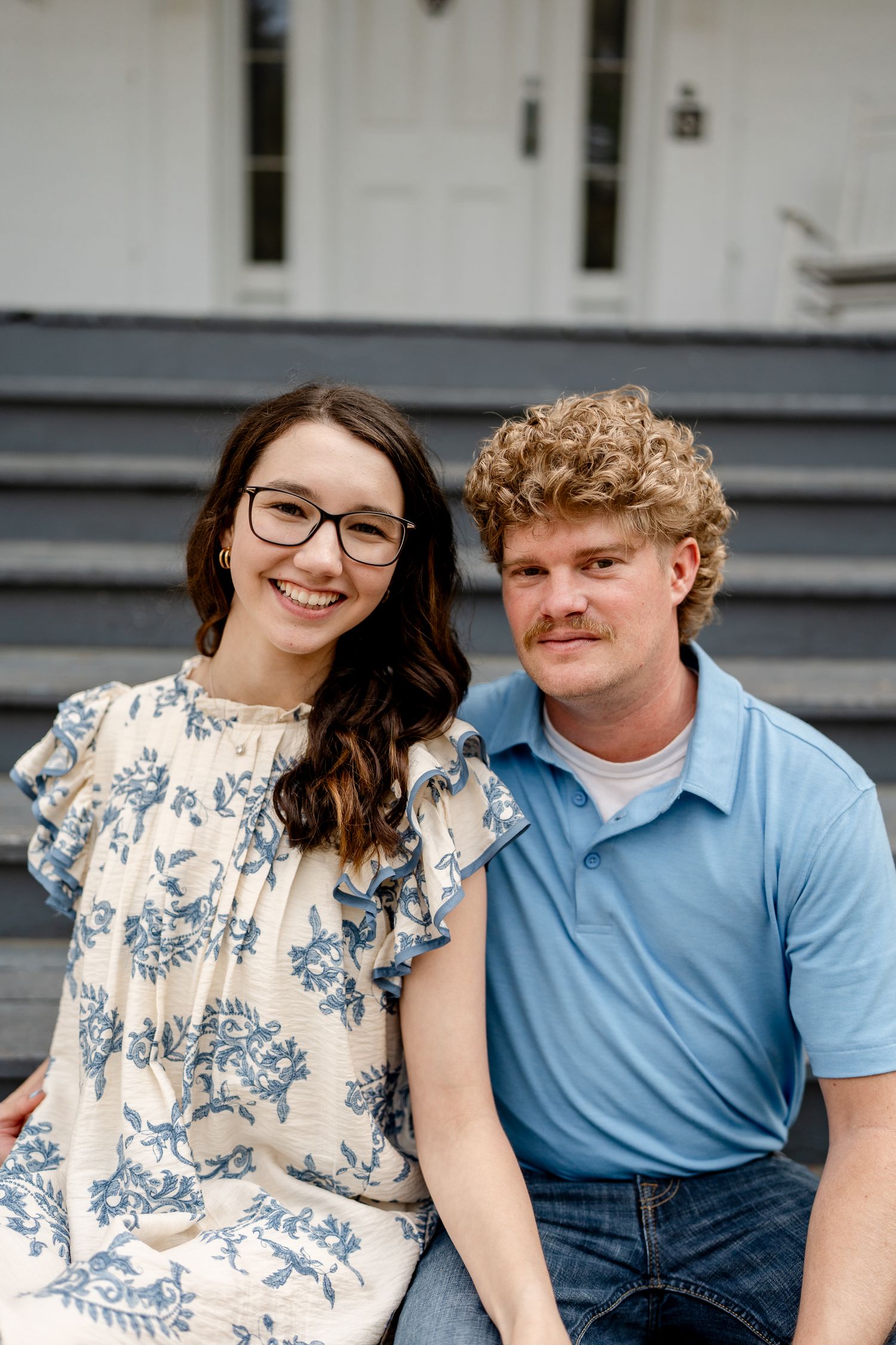 A couple sits close together on gray steps, smiling at the camera.