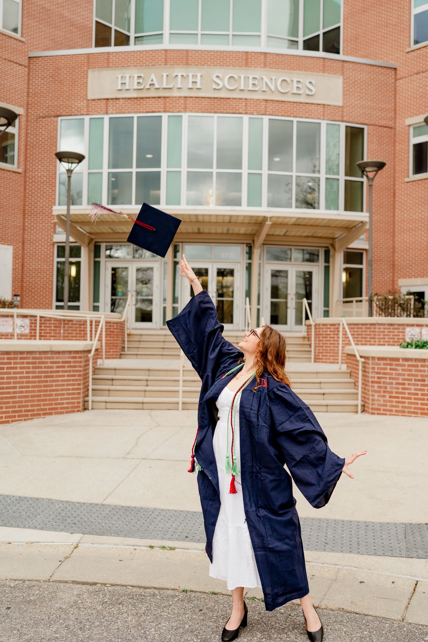 Graduate tosses cap in celebratory sequence outside brick Health Sciences building.