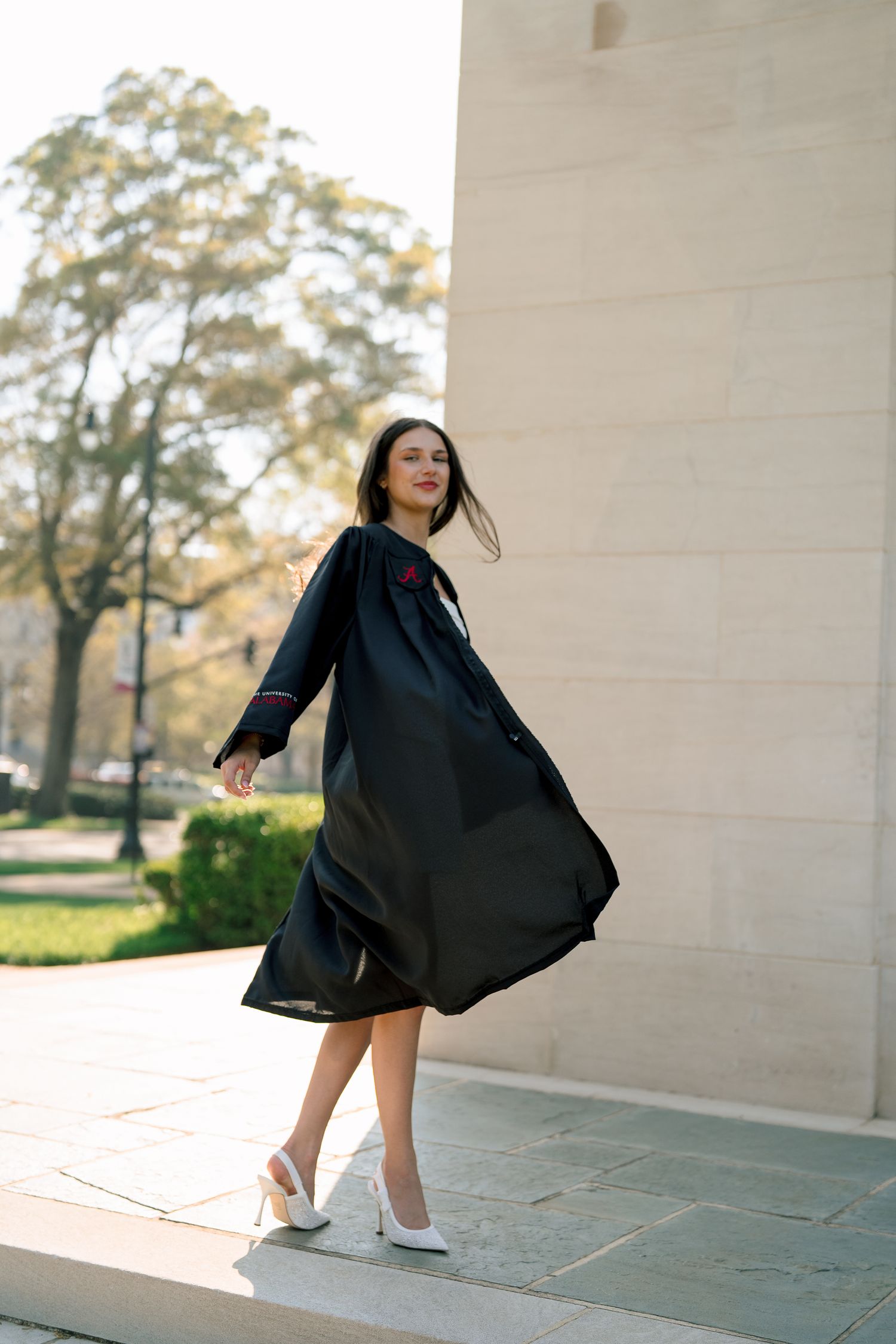 A person in a flowing black dress twirls gracefully in front of a white stone wall during golden hour.