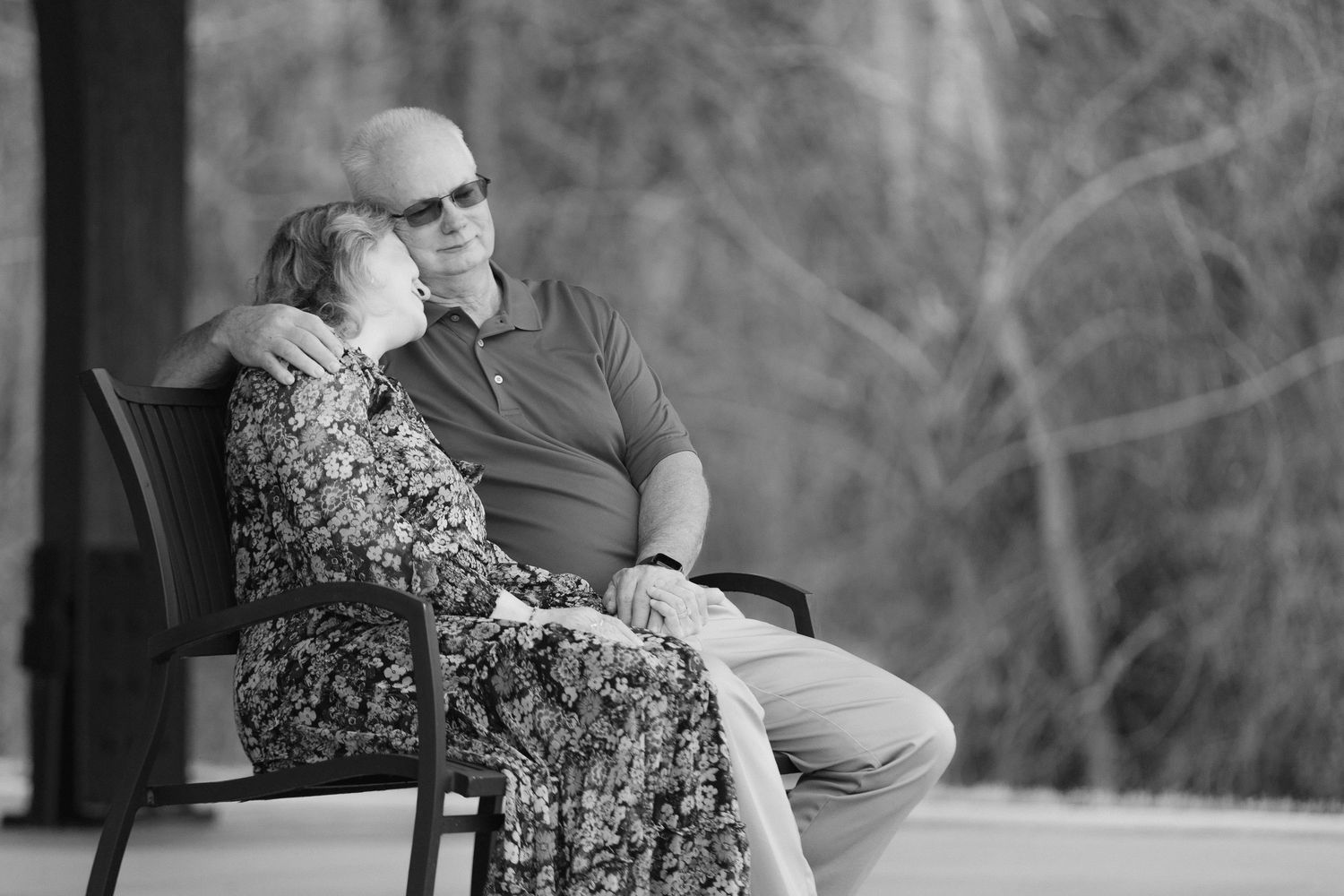 Elderly couple sitting close together on a bench, sharing a tender moment outdoors.
