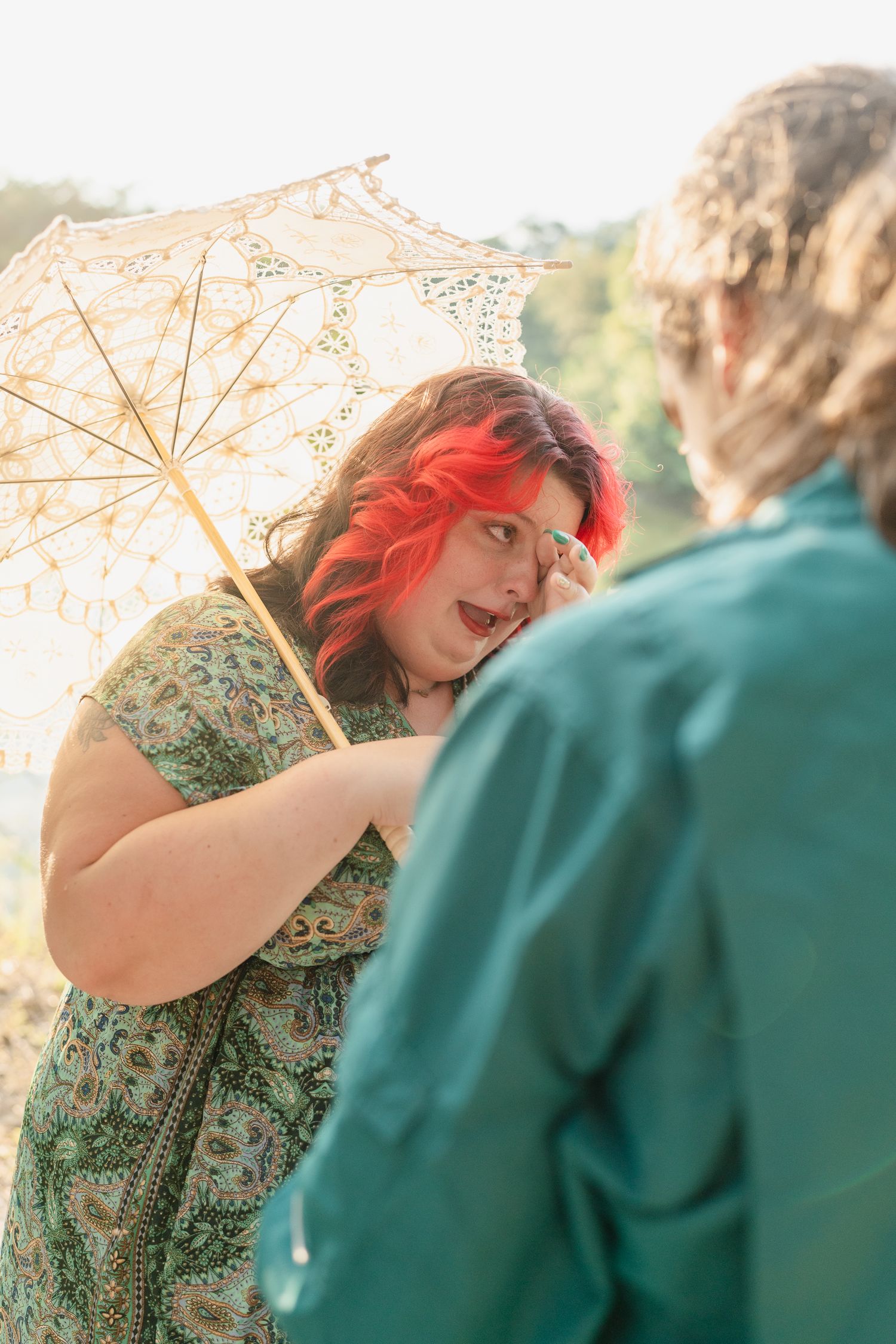 Two people share a joyful moment outdoors with a delicate lace parasol against natural scenery.
