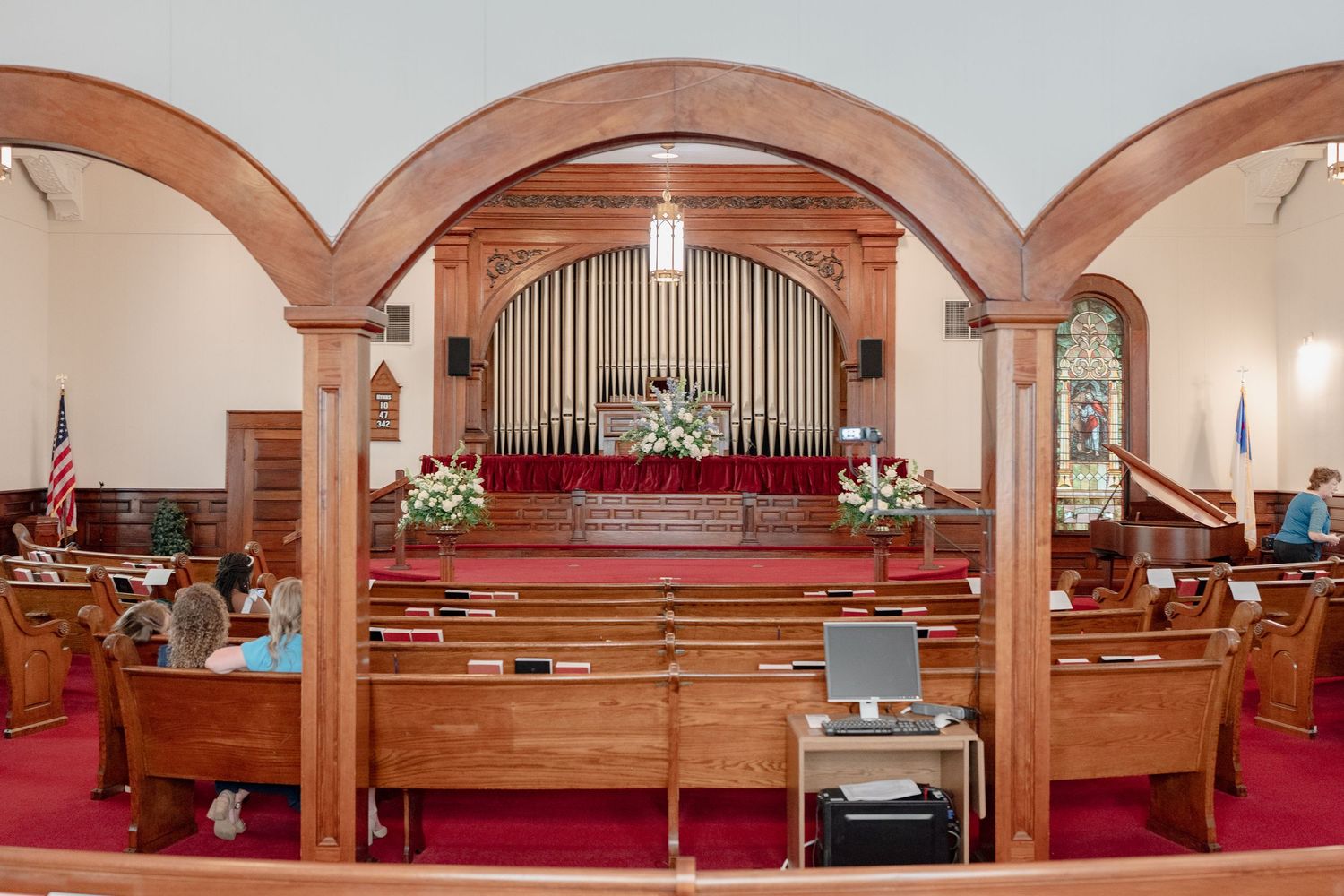 Traditional church sanctuary interior with wooden pews, red carpet, and pipe organ at the front.