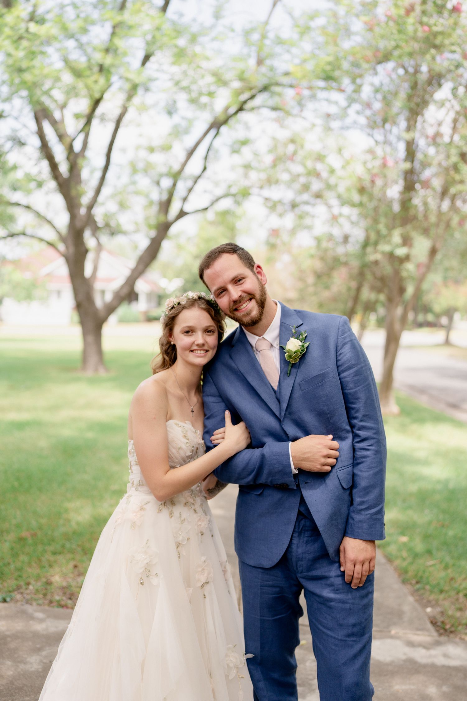 A wedding couple shares intimate moments in a sunlit garden setting with trees in the background.