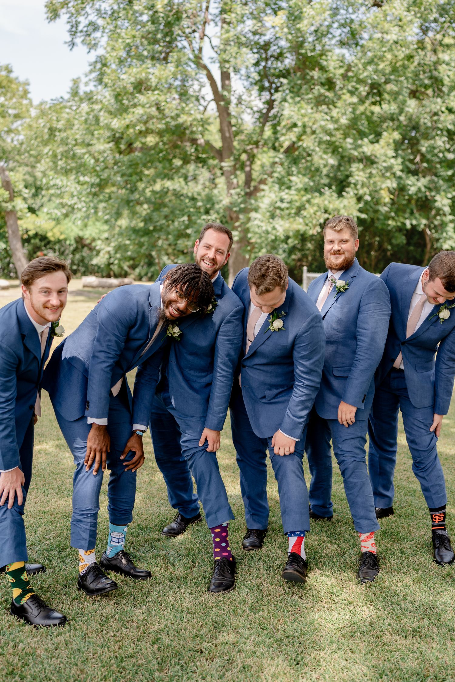 Groomsmen in navy blue suits showing off their colorful patterned socks in a fun outdoor photo.