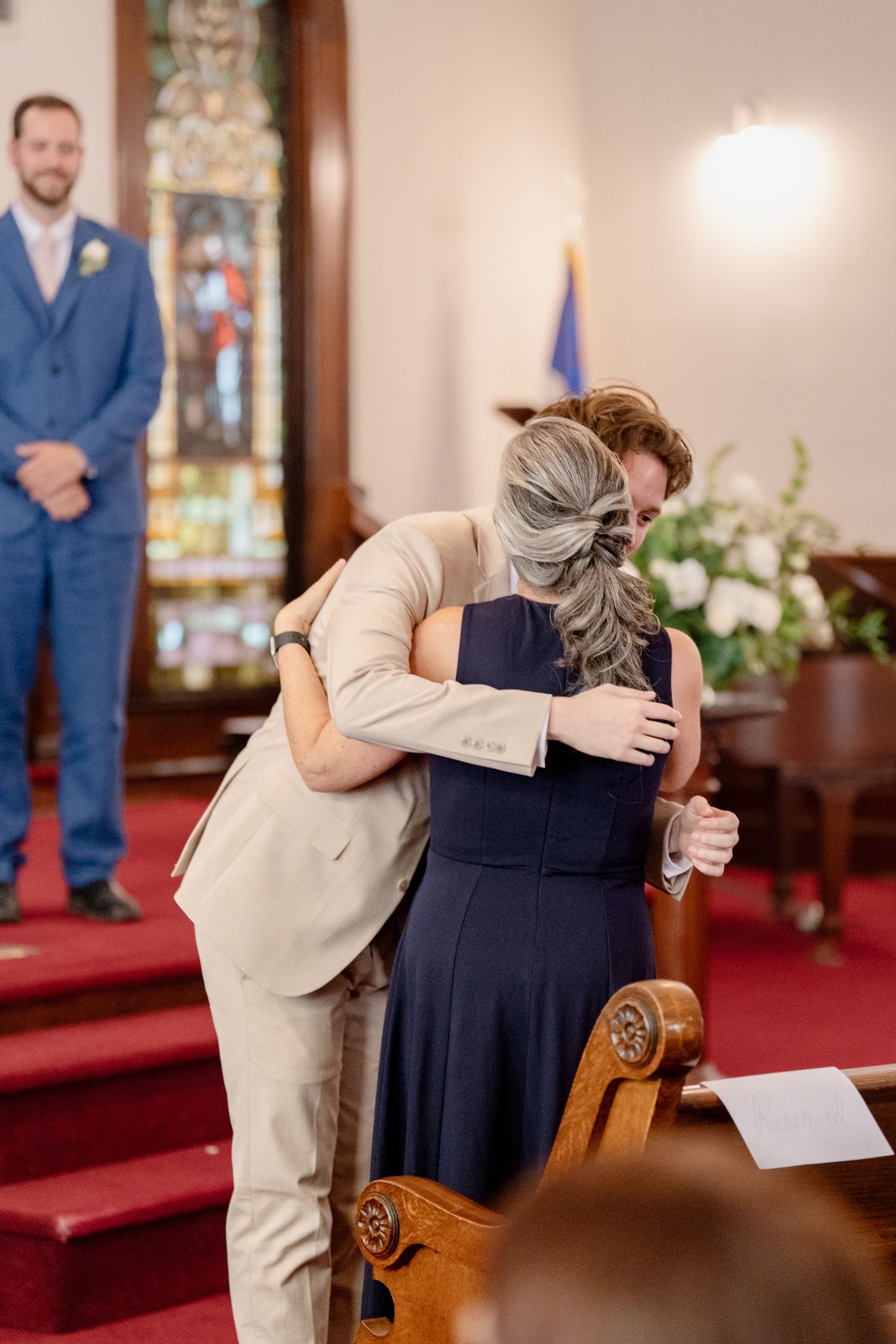 Emotional moment shared between wedding attendees embracing in a church sanctuary.