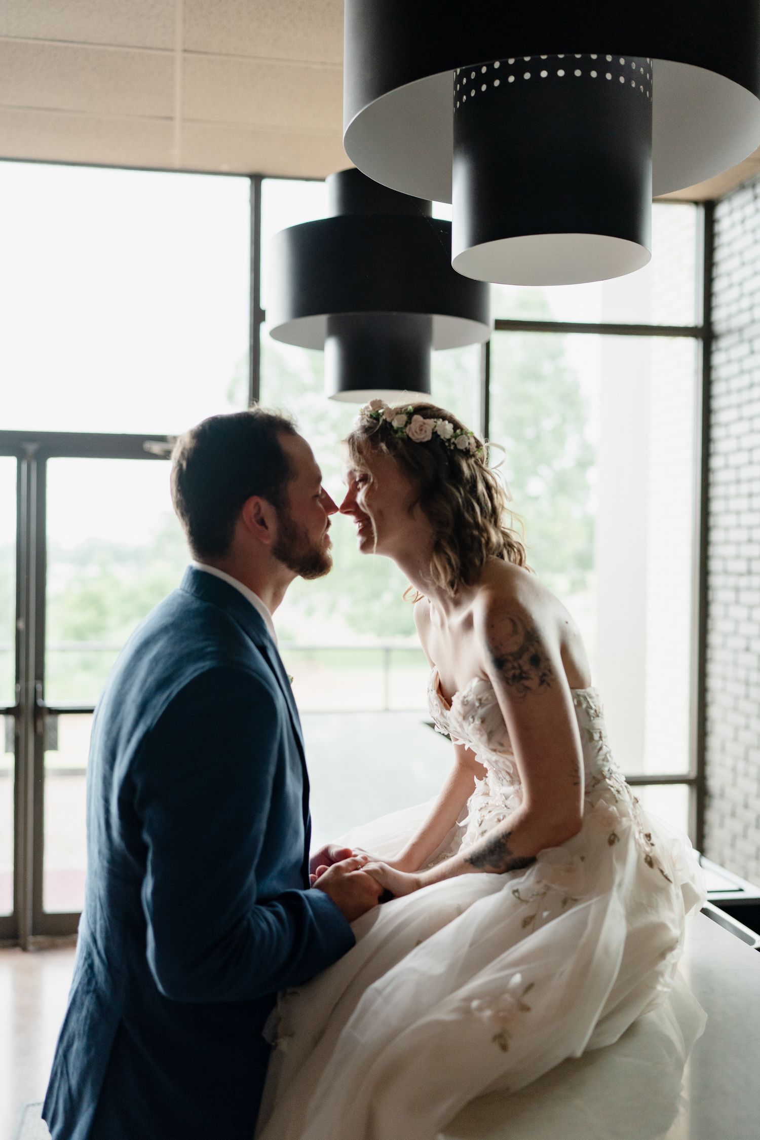 A couple shares an intimate moment in a modern venue with black pendant lights and floor-to-ceiling windows.