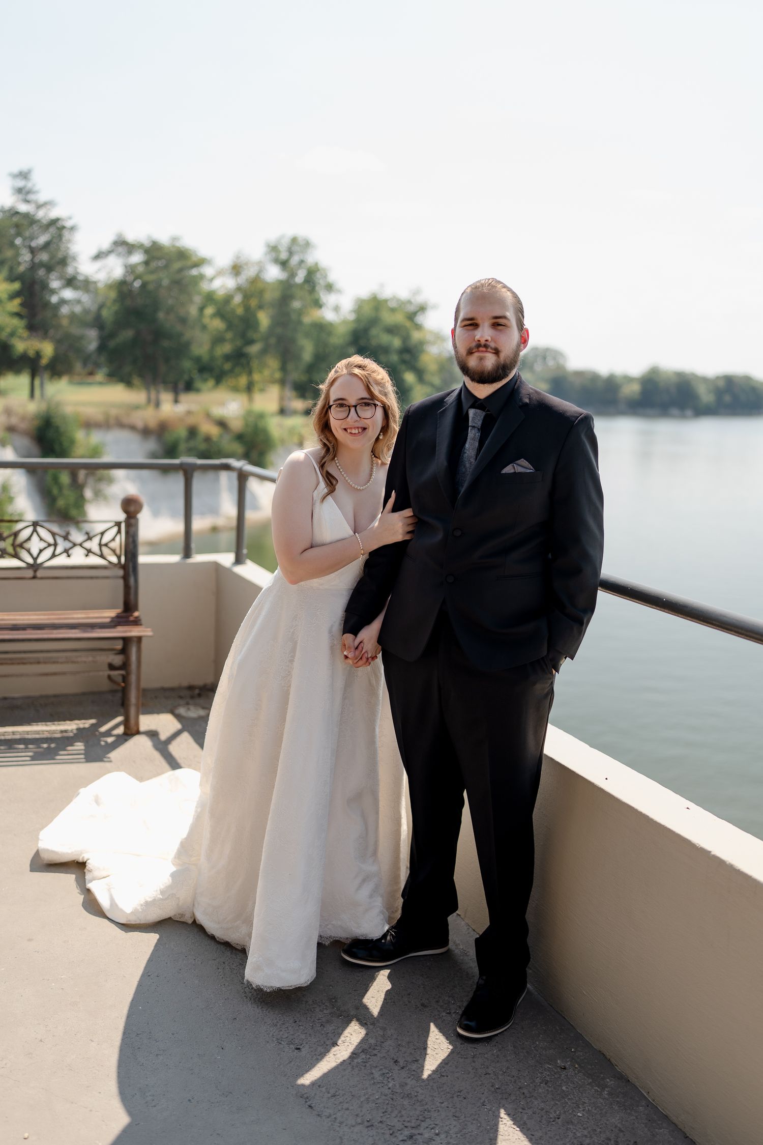 Joyful wedding couple sharing laughs on a waterfront balcony during their special day.