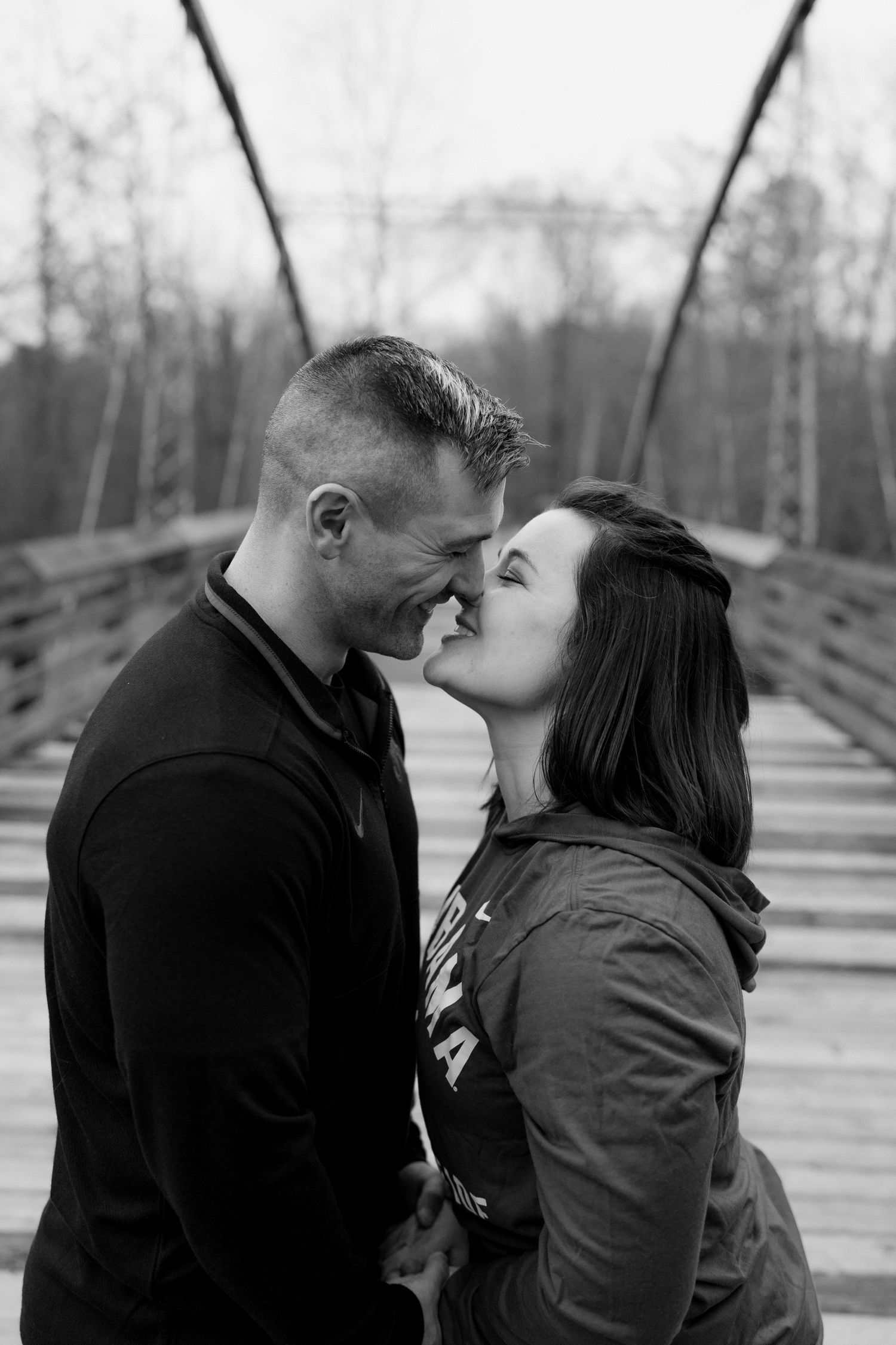 A couple shares intimate moments together on a wooden bridge in black and white tones.