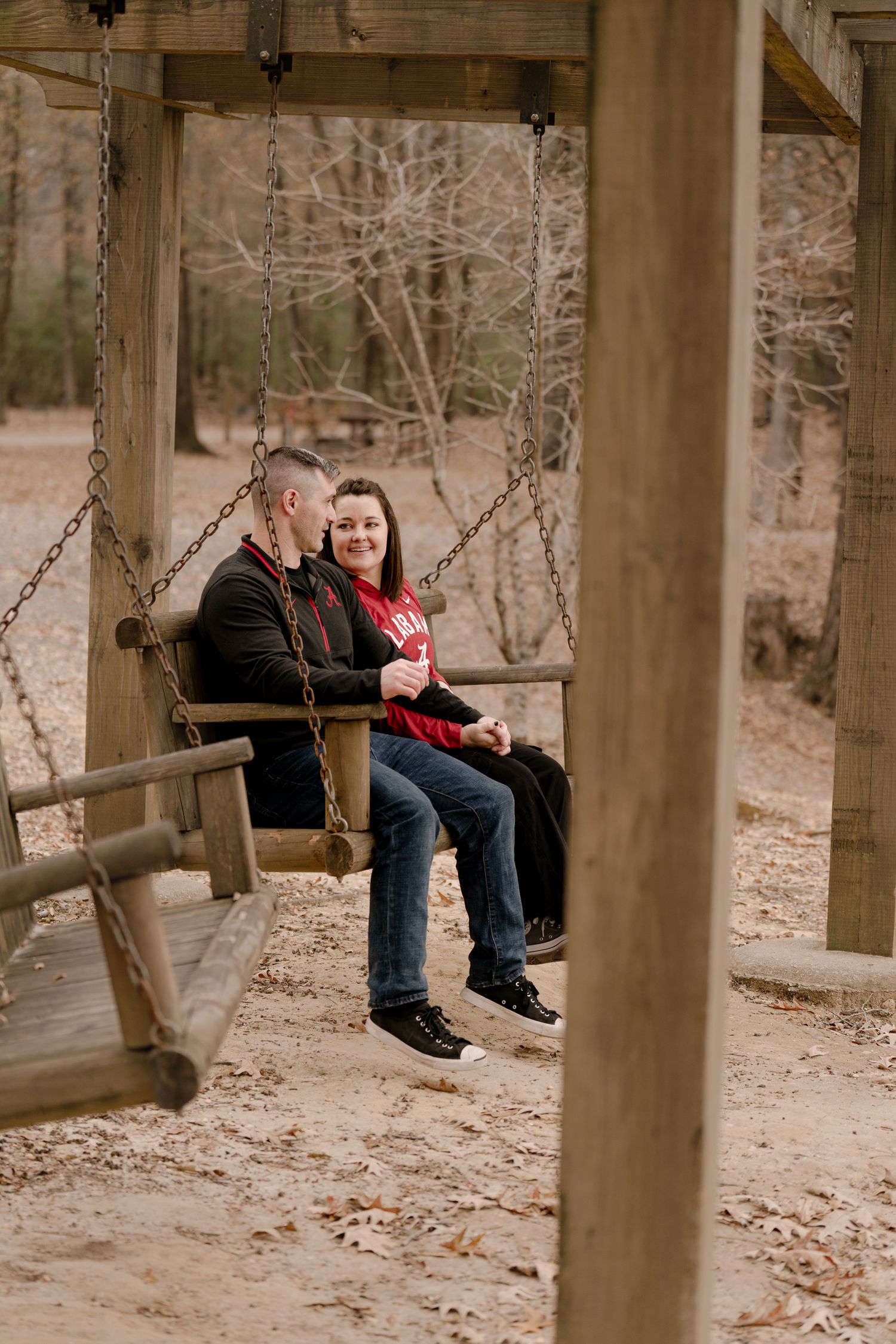 A couple sits together on a rustic wooden porch swing in a peaceful outdoor setting during autumn.