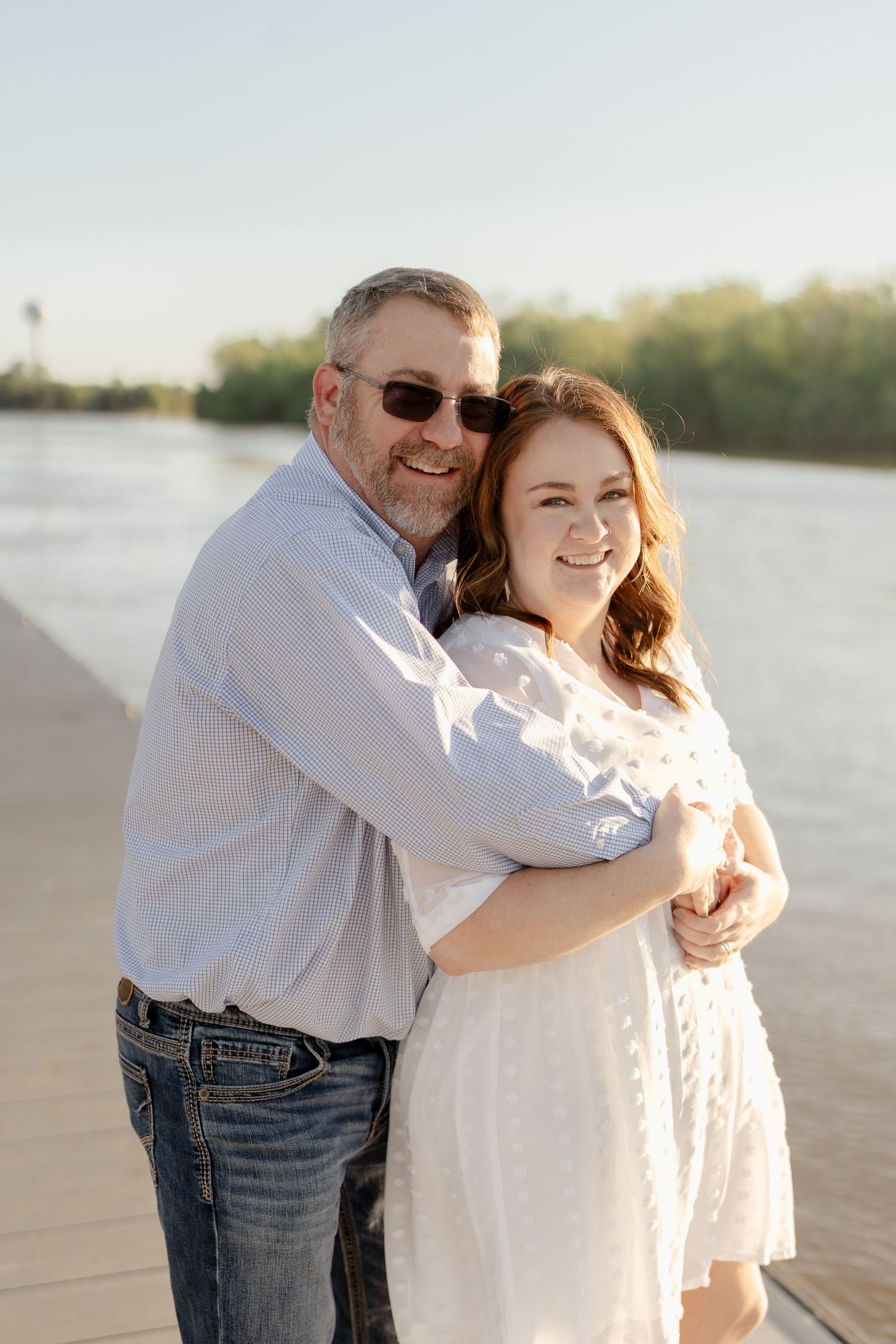 Two people embrace while sharing a happy moment on a sunlit pier.