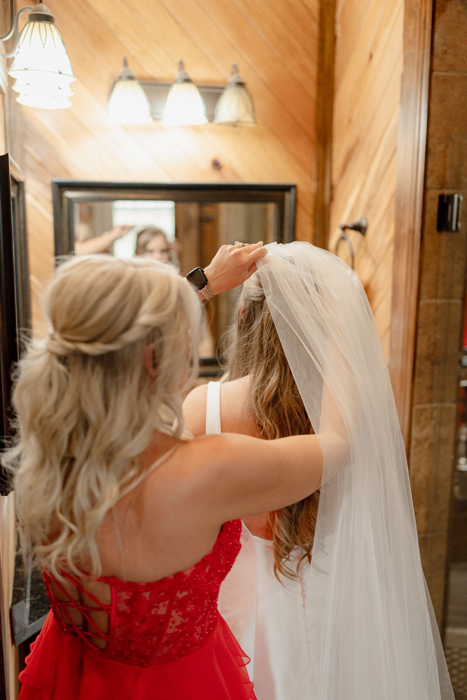 Wedding dress preparations with a red lace bridesmaid dress and flowing white veil in a wooden cabin.