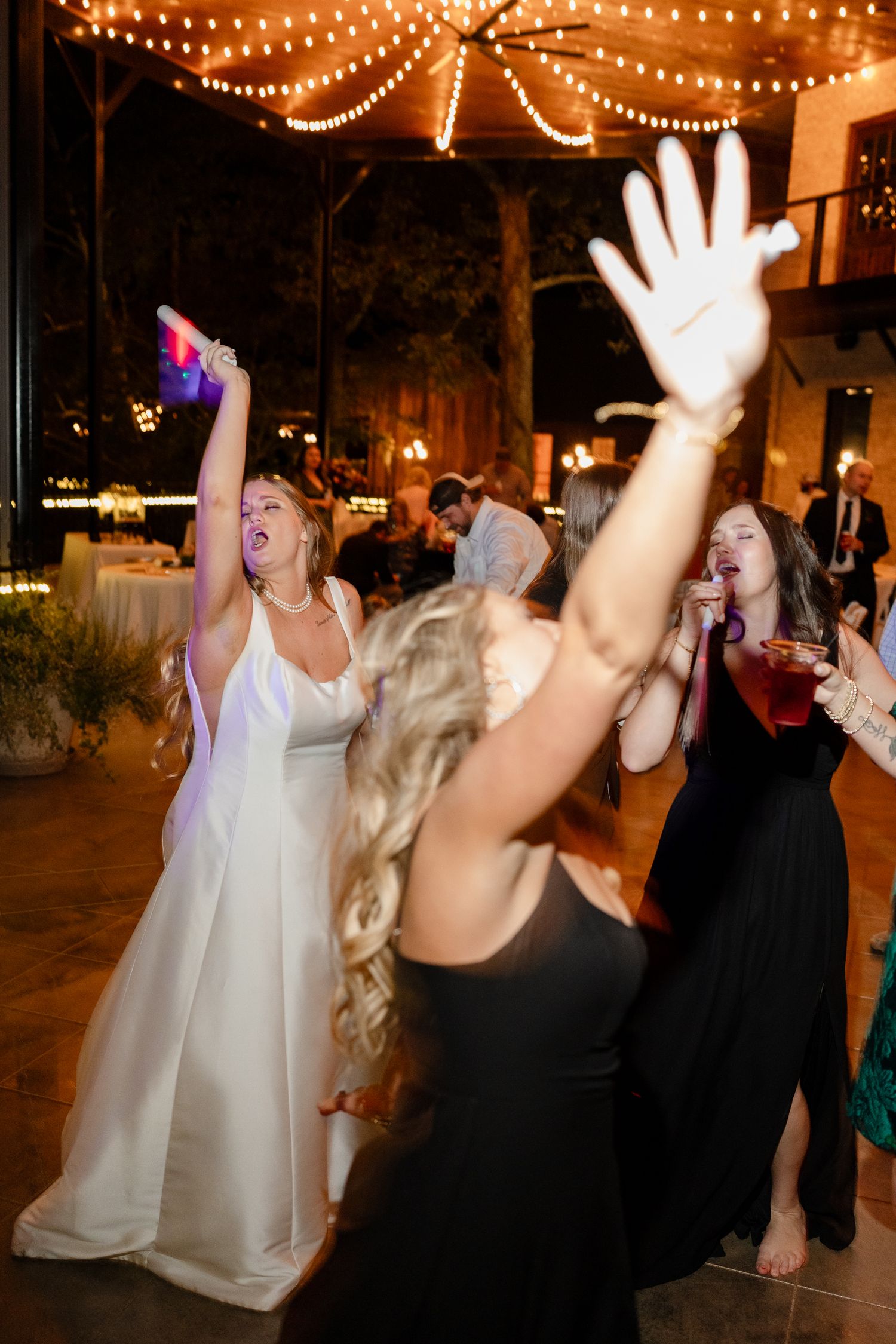 Wedding reception dance party with string lights and guests dancing with hands in the air.