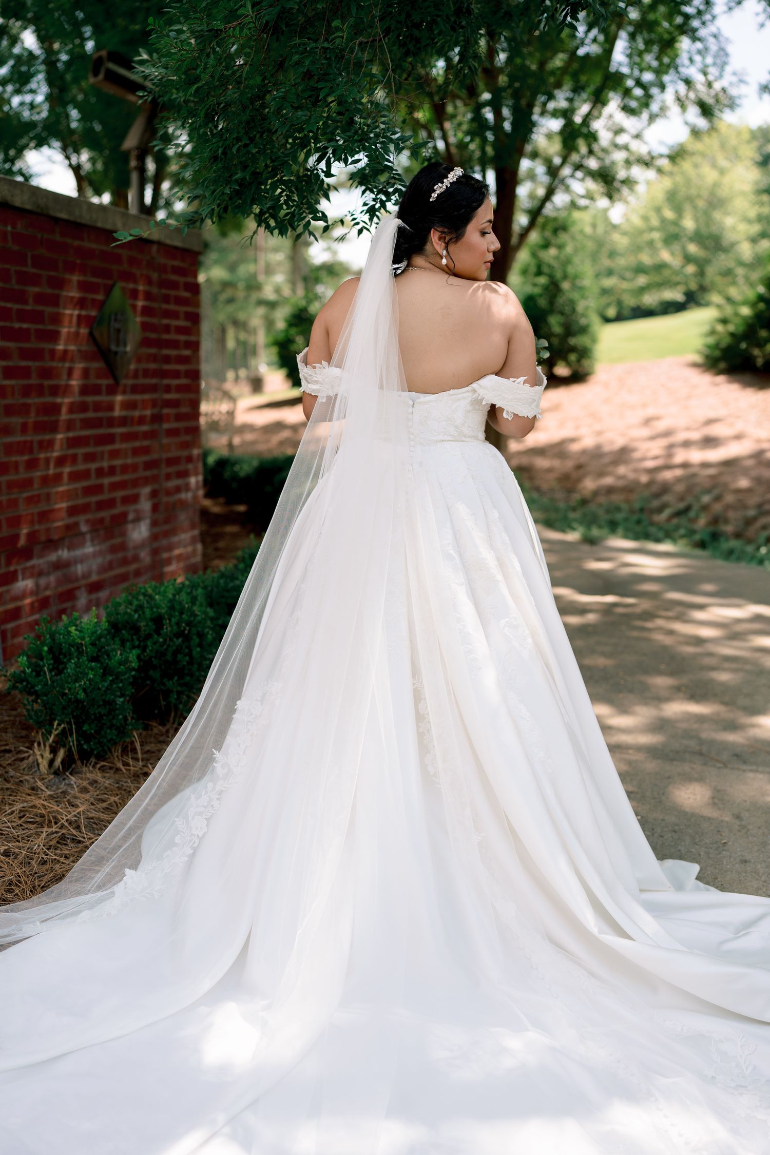 A flowing white wedding dress train cascades across a brick pathway in an outdoor garden setting.