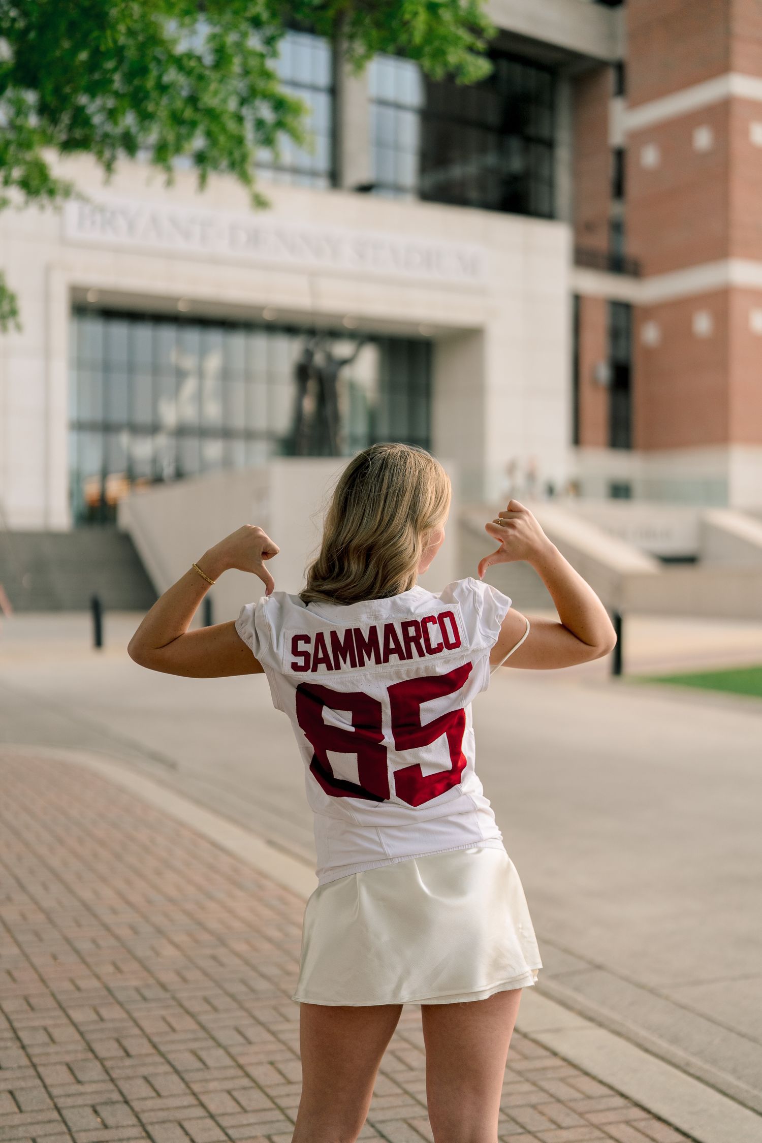 A student wearing a white jersey with number 85 poses in front of a campus building.