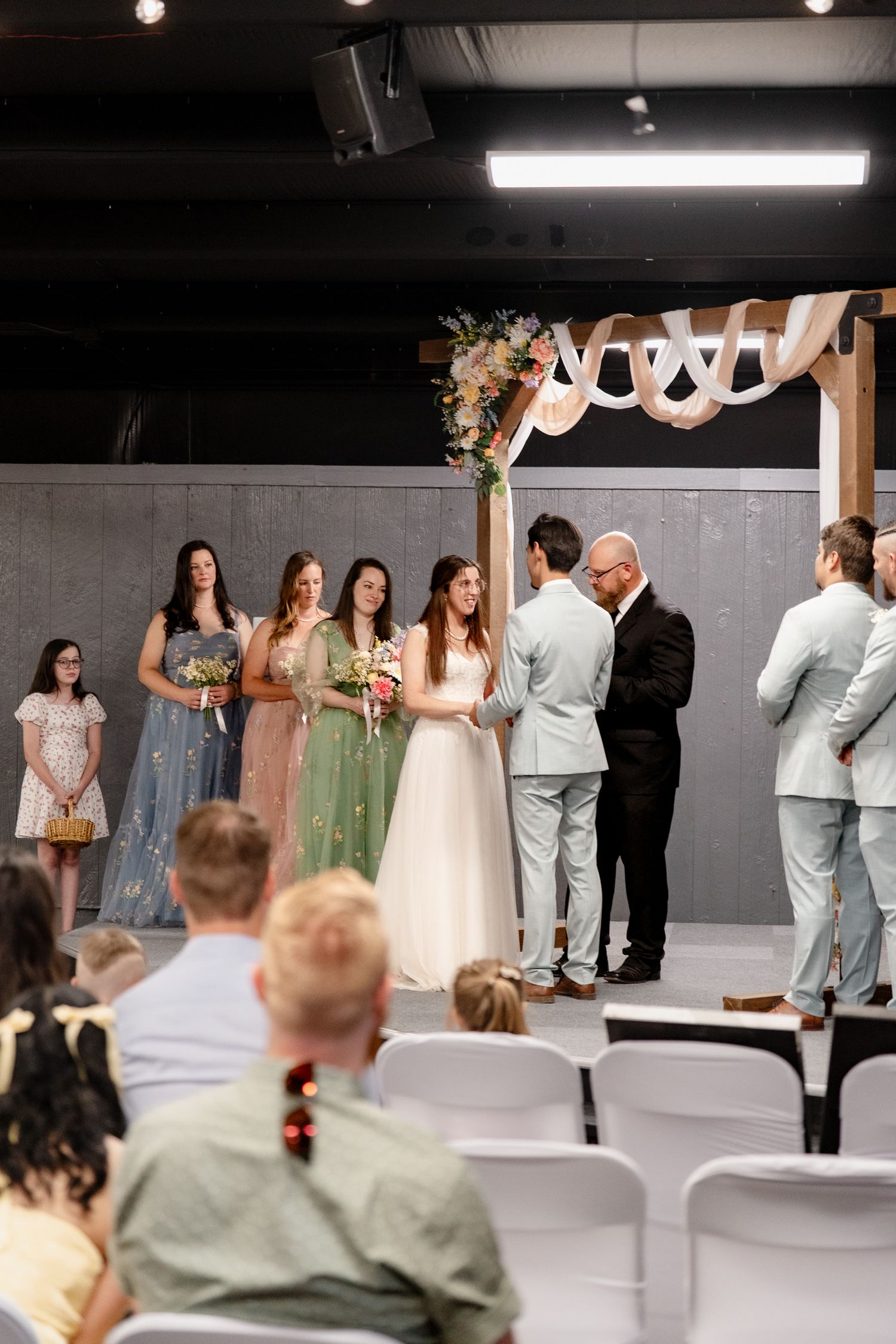 Wedding ceremony with bridesmaids in pastel dresses and groomsmen in light suits standing before white chairs.