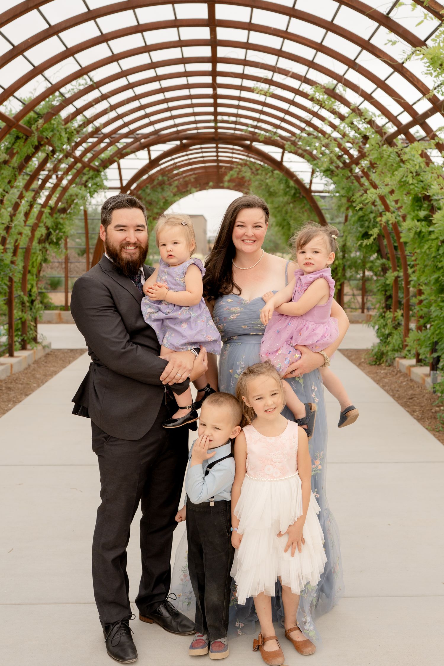 Group photo of adults with small children gathered under an arched greenhouse structure.