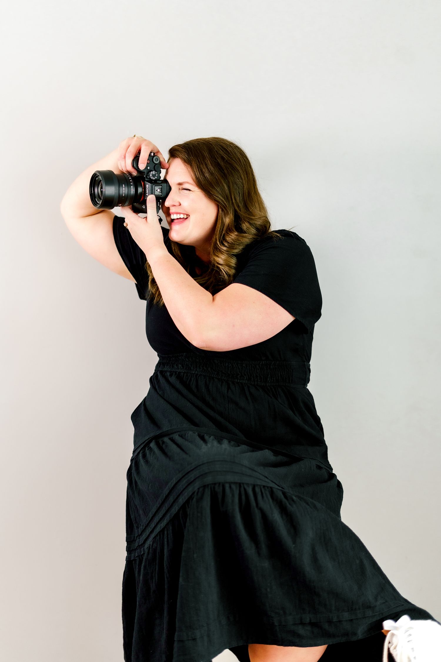 A person in a black dress shows various ways of holding and using a professional camera.