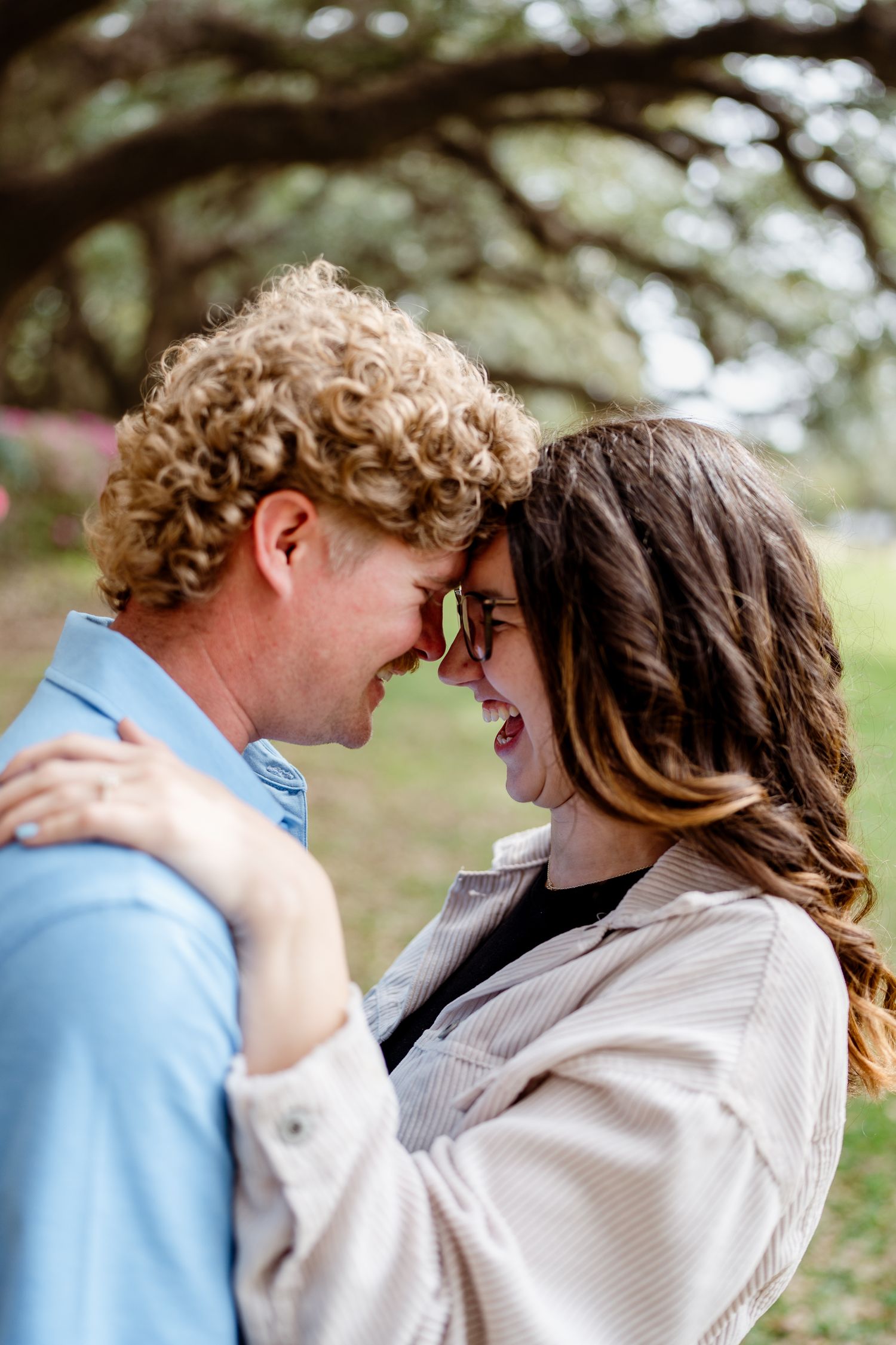 A playful moment captured between two people laughing under oak trees.
