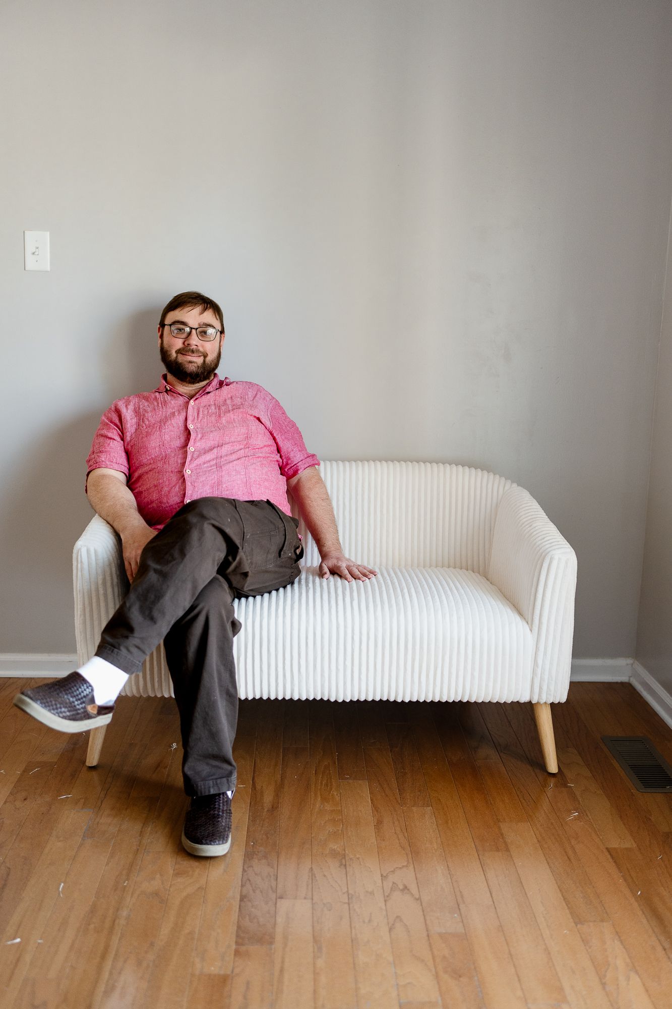 Person in pink shirt and gray pants relaxes on modern white loveseat.