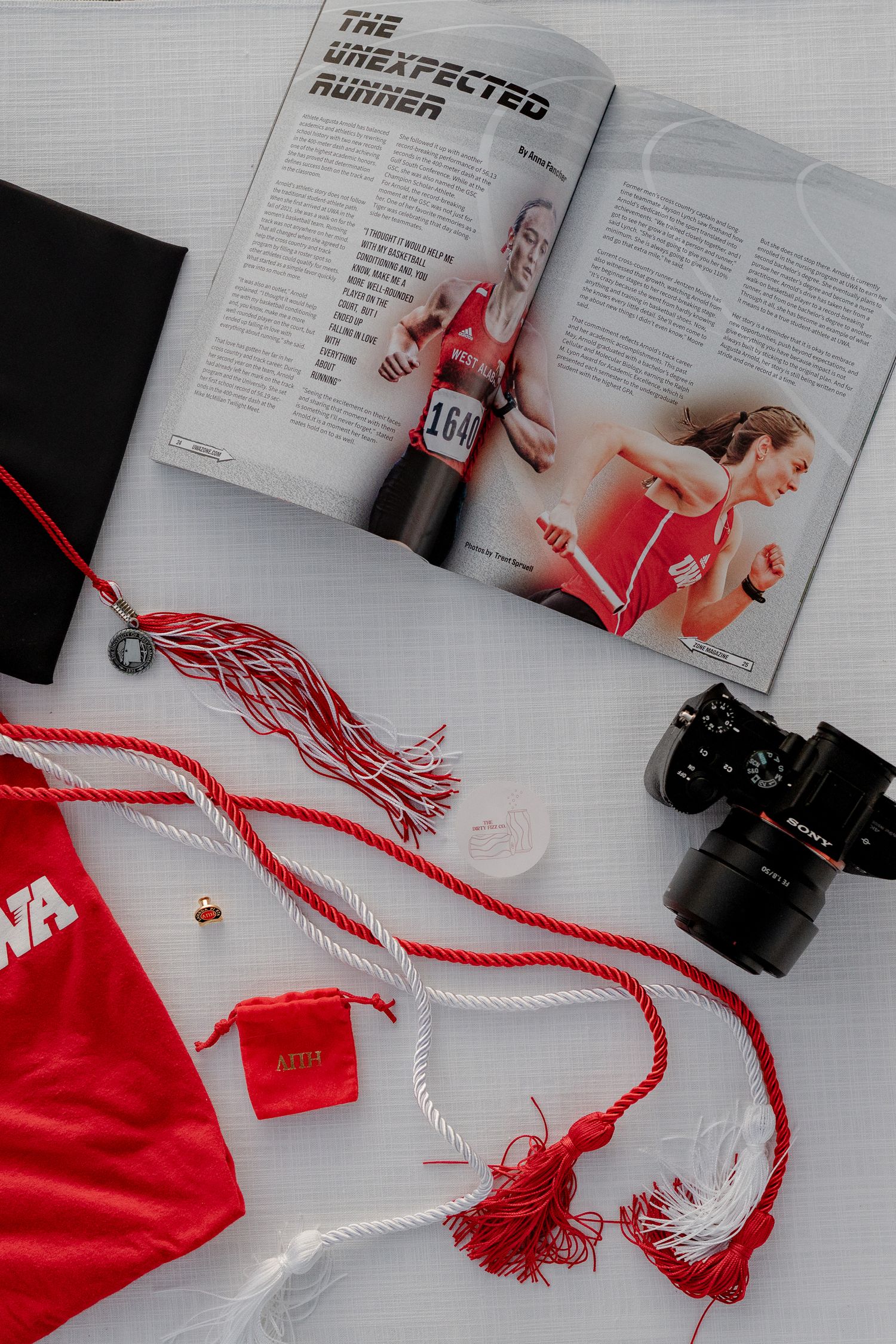 Magazine pages laid flat with red graduation cords and camera creating an artistic composition in black and white tones.