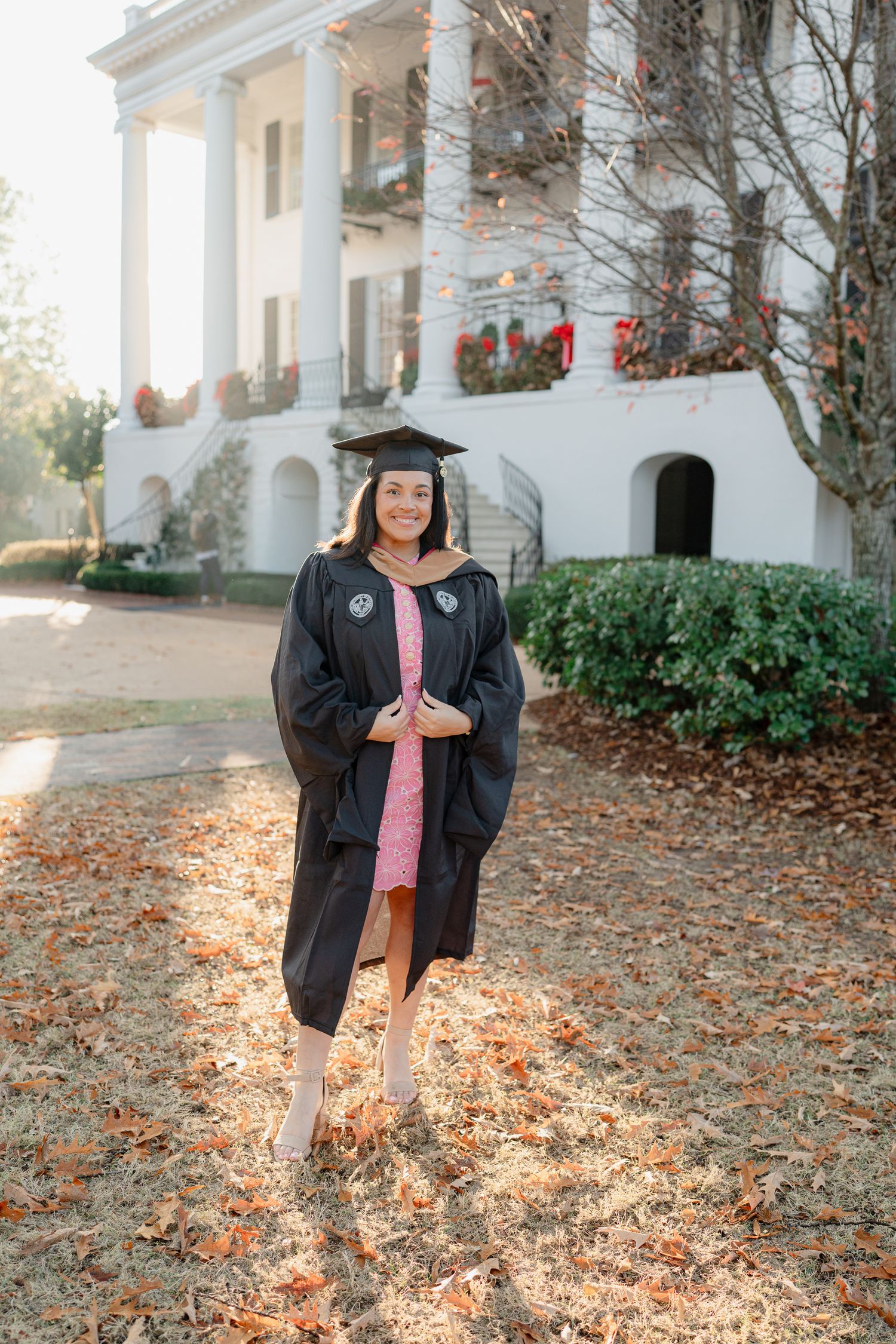 Graduate in black cap and gown posing in front of a stately white building with columns.