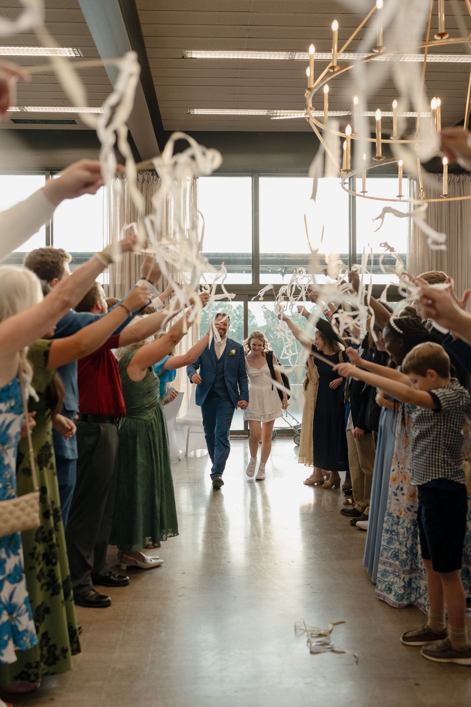 Wedding guests stand in rows with raised arms during a celebratory moment in a bright reception hall.
