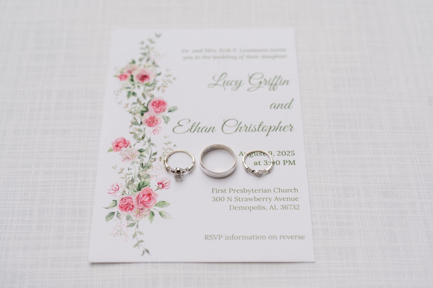 Elegant wedding invitation with delicate pink floral design and silver rings on white textured background.