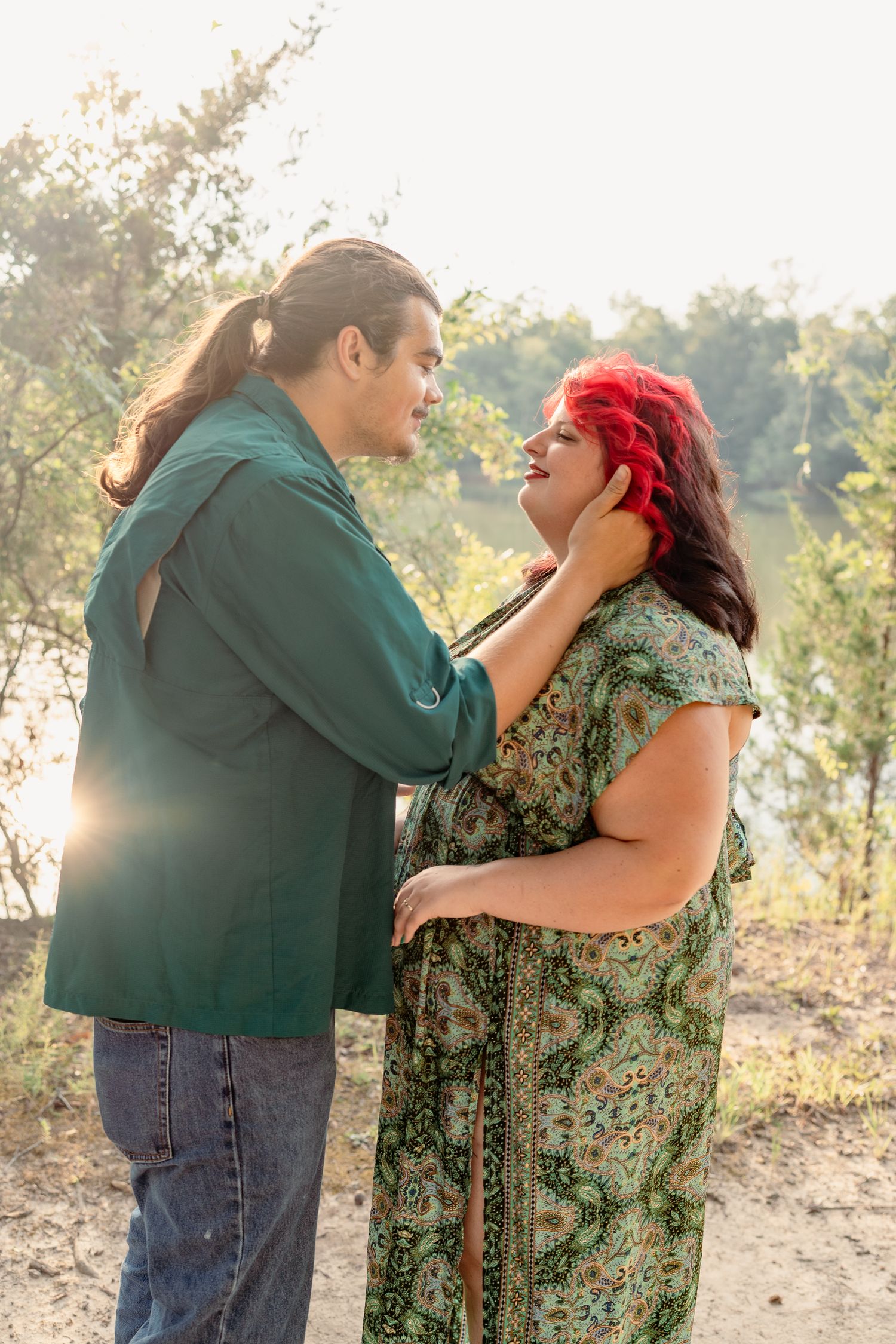 A tender romantic moment between two people in a sunlit outdoor setting, with natural scenery in the background.