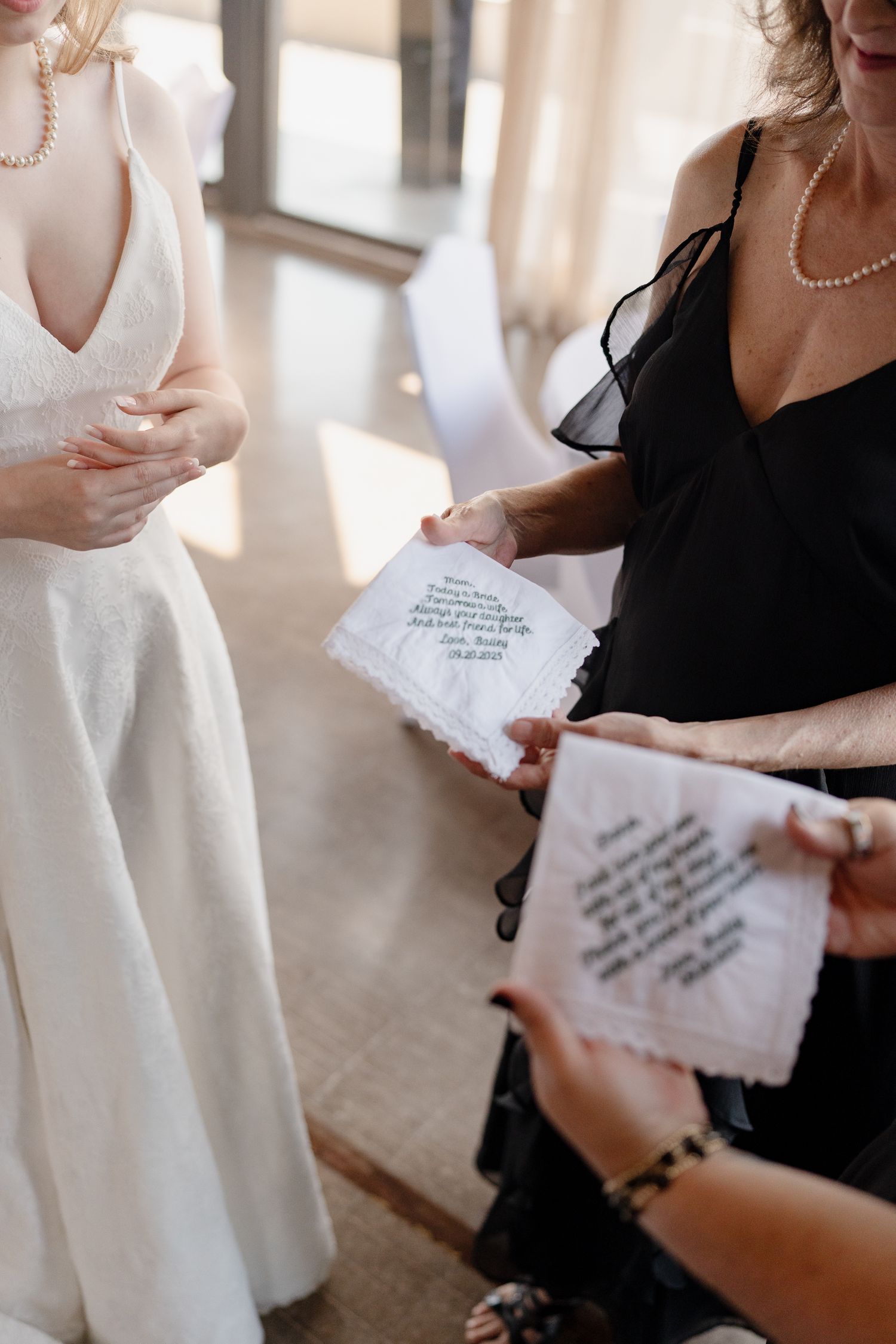 A person in a black dress reads a handwritten note next to someone wearing a white dress in a sunlit room.