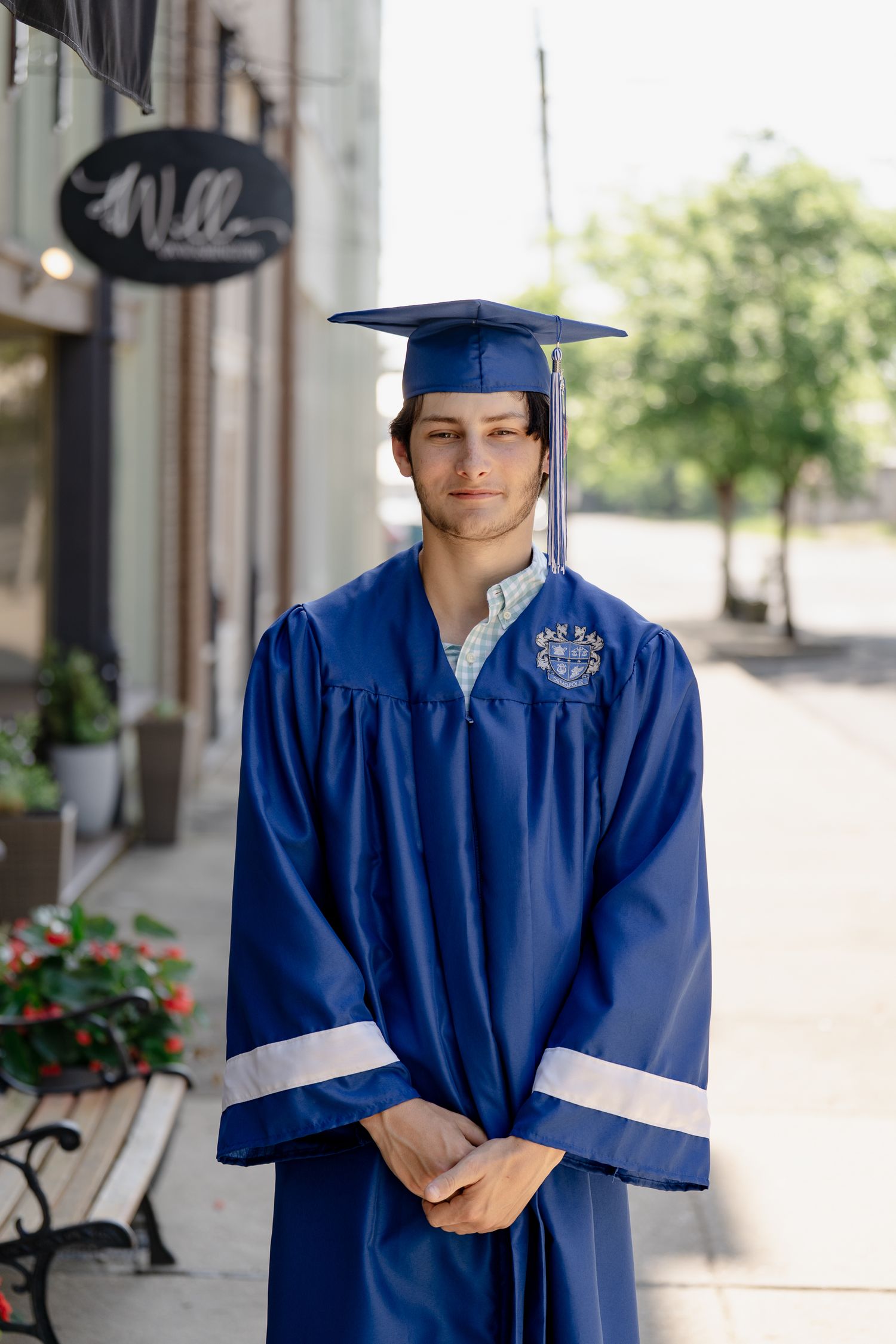 Graduate in royal blue regalia poses on city sidewalk near storefront.